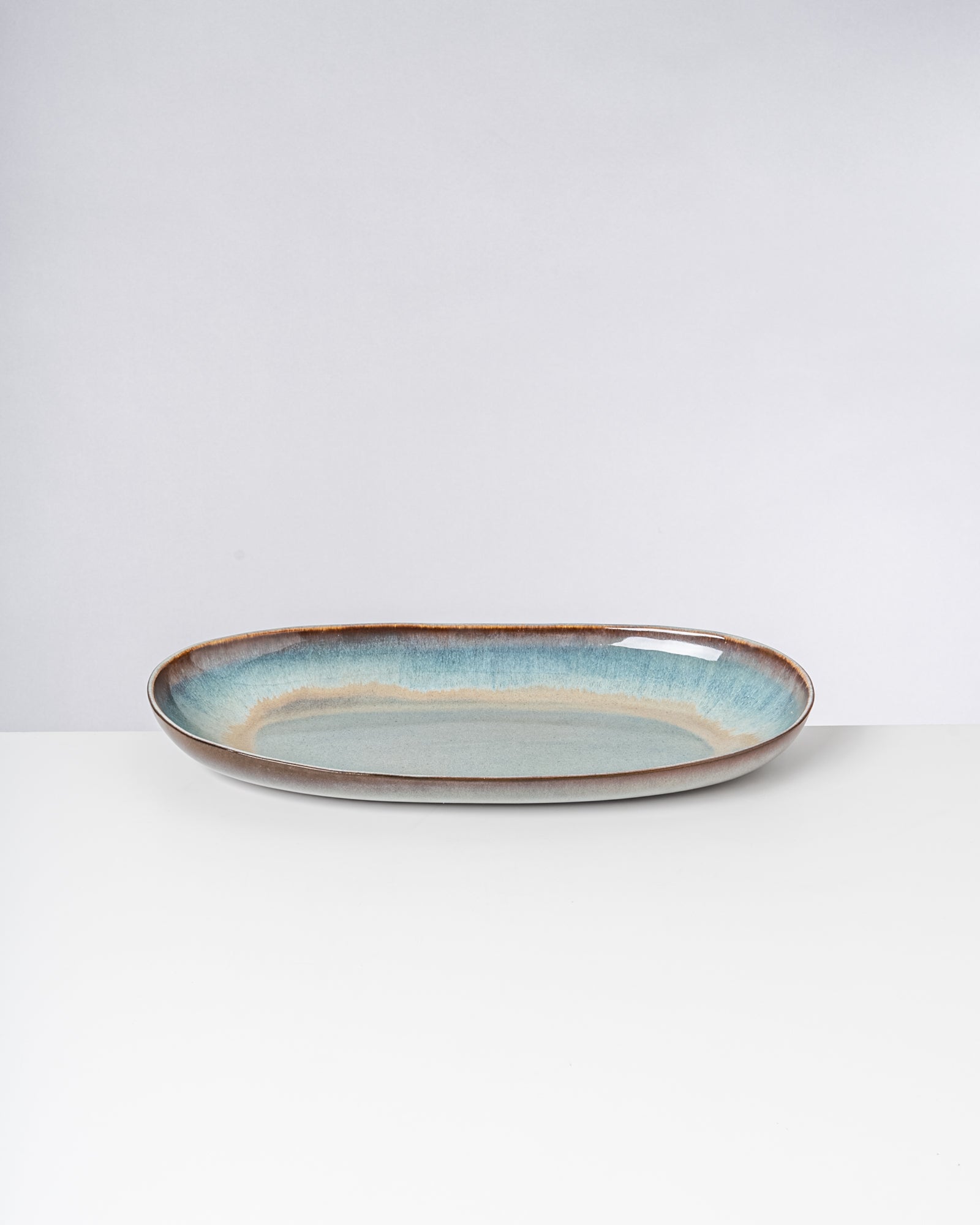 Länglicher, flacher Keramikteller mit blau-grüner Glasur auf einem weißen Hintergrund.