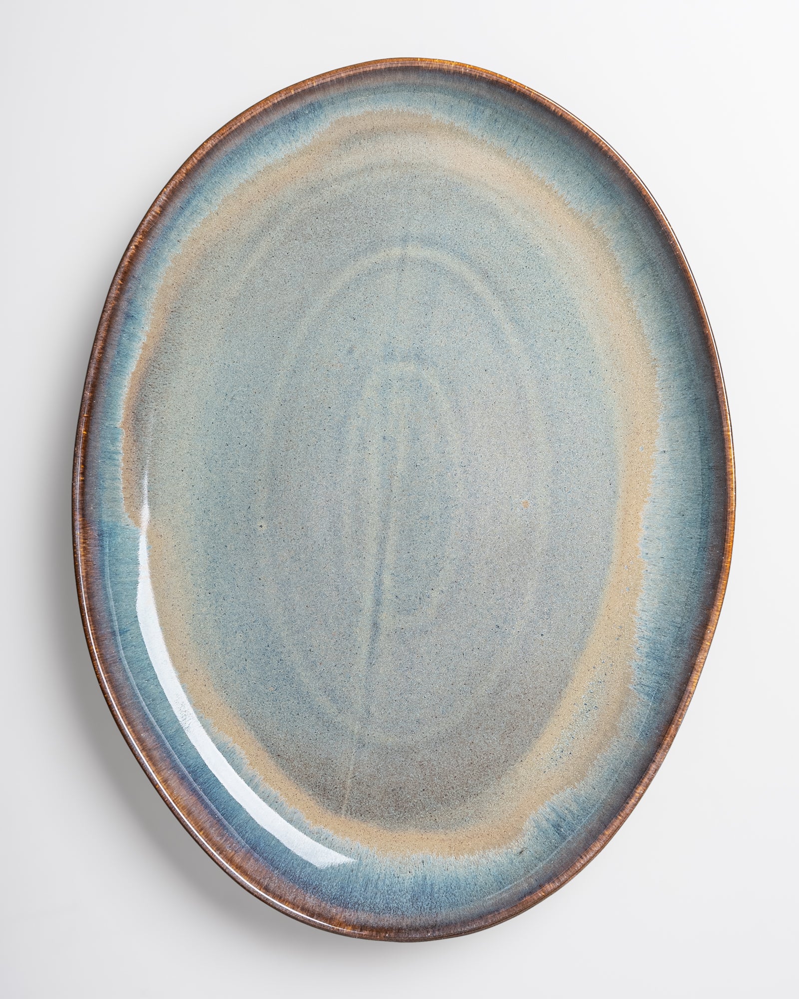 Ein ovaler Keramikteller in Blautönen mit einem braunen Rand auf weißem Hintergrund.
