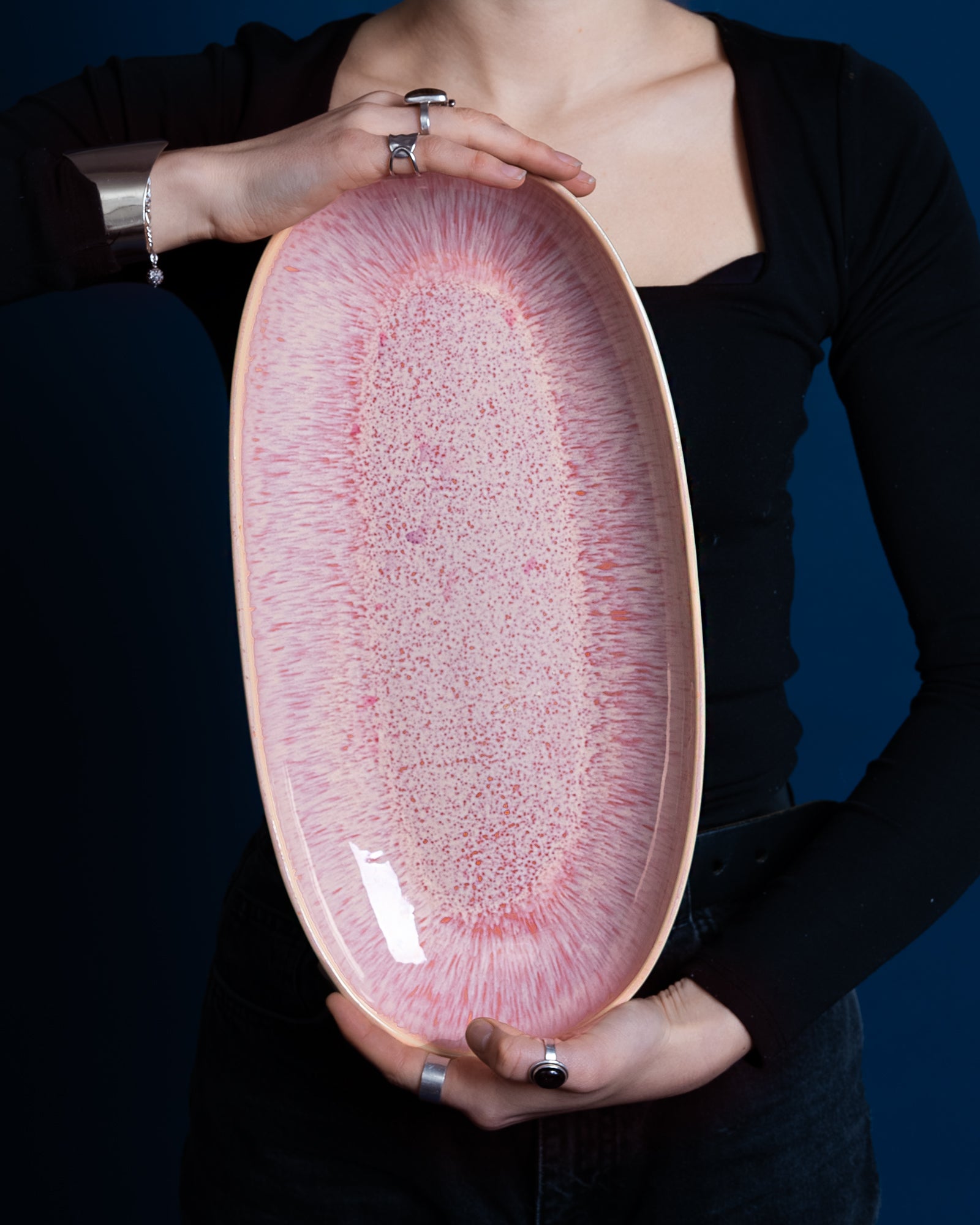Person hält ein großes ovales, rosafarbenes Teller mit blassrosa Muster vor einem dunkelblauen Hintergrund.