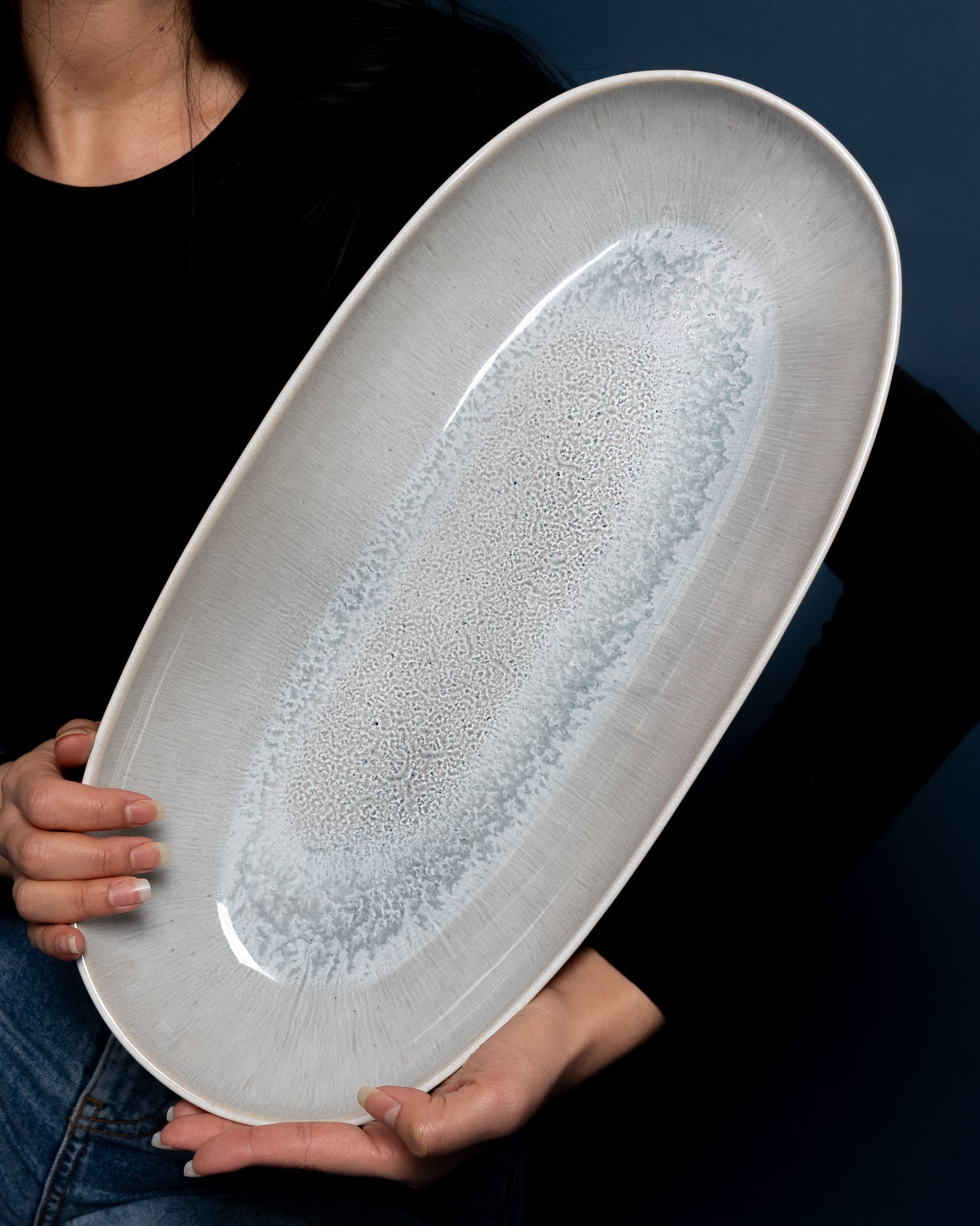 Person hält eine große, ovale, weiß-blaue Keramikplatte vor einem dunkelblauen Hintergrund.