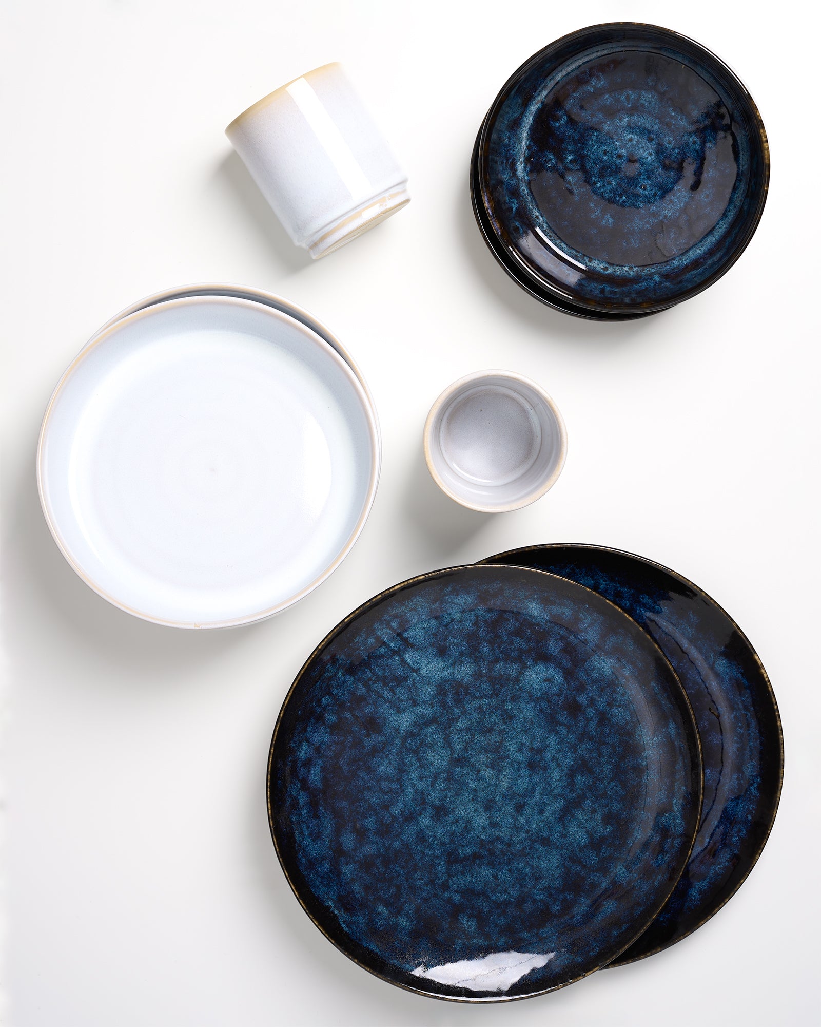 Verschiedene Keramikteller und -tassen in weiß und blau auf einem weißen Hintergrund angeordnet.