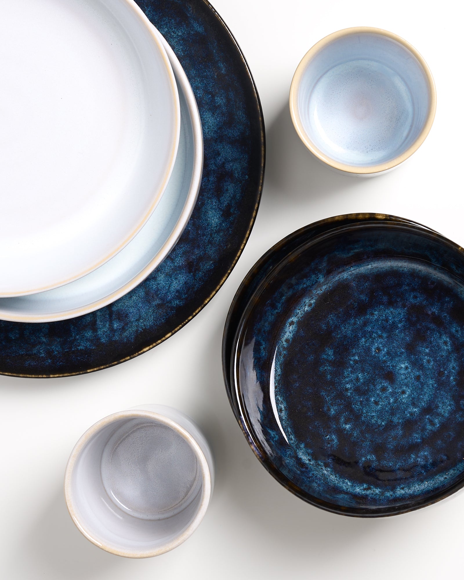 Verschiedene blaue und weiße Keramikgeschirrteile, darunter Teller und Schalen, auf weißem Hintergrund angeordnet.