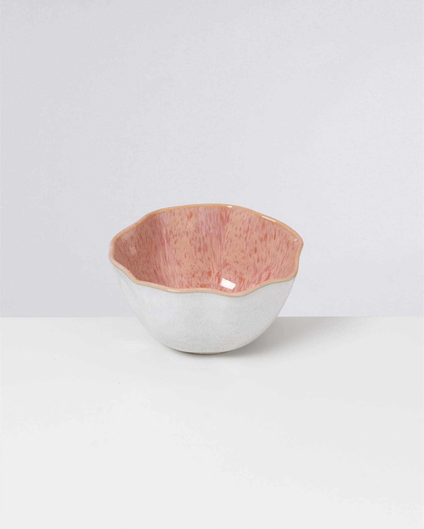 Weiße, bauchige Keramikschale mit welligem, rosa geflecktem Rand, auf weißem Hintergrund.