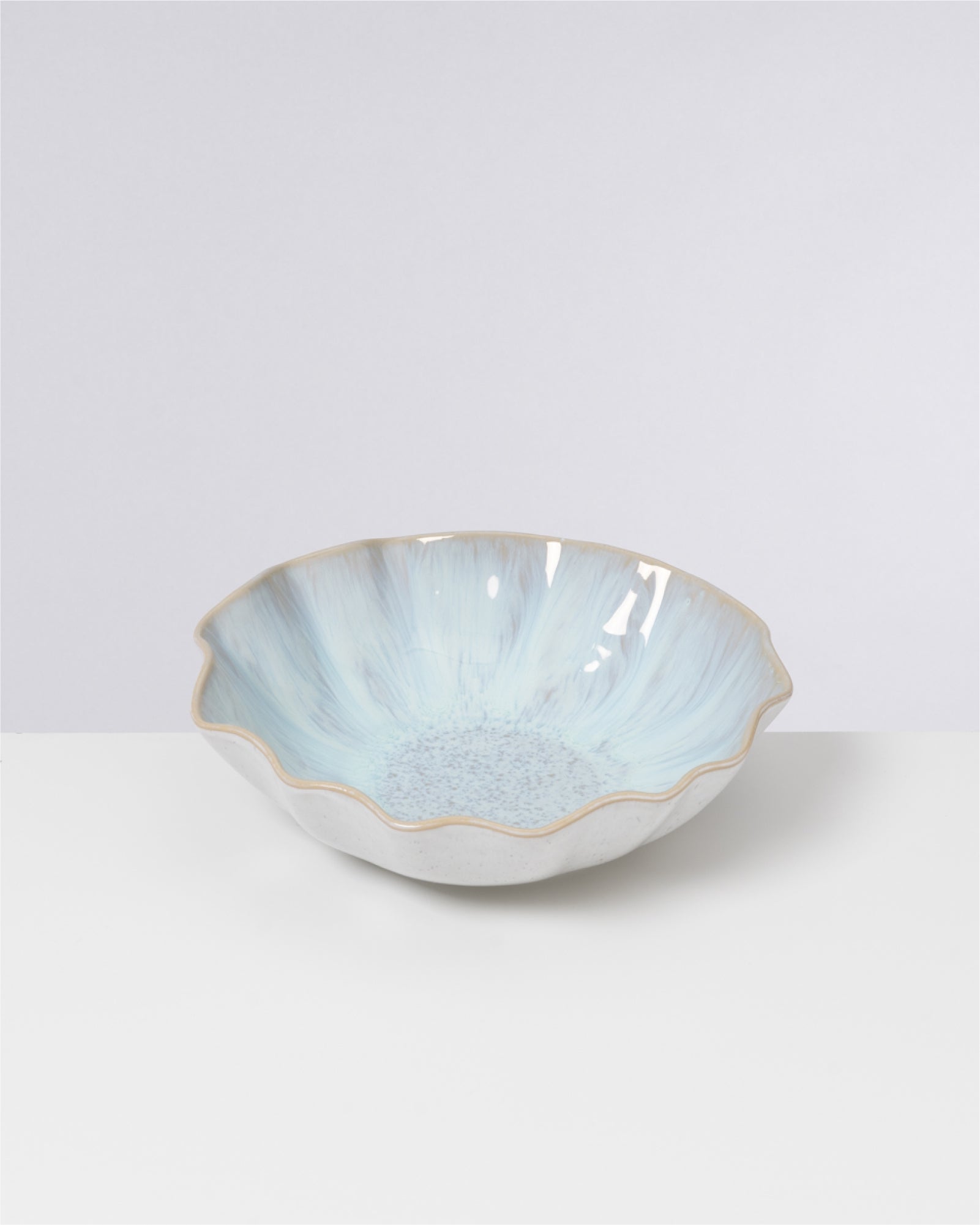 Eine pastellblaue, blütenförmige Schale mit welligem Rand steht auf einem weißen Untergrund.