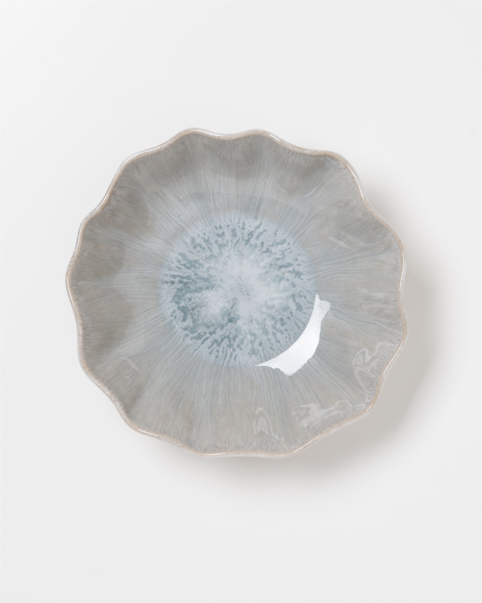 Grauer, blütenförmiger Teller mit bläulichem Muster in der Mitte auf weißem Hintergrund.