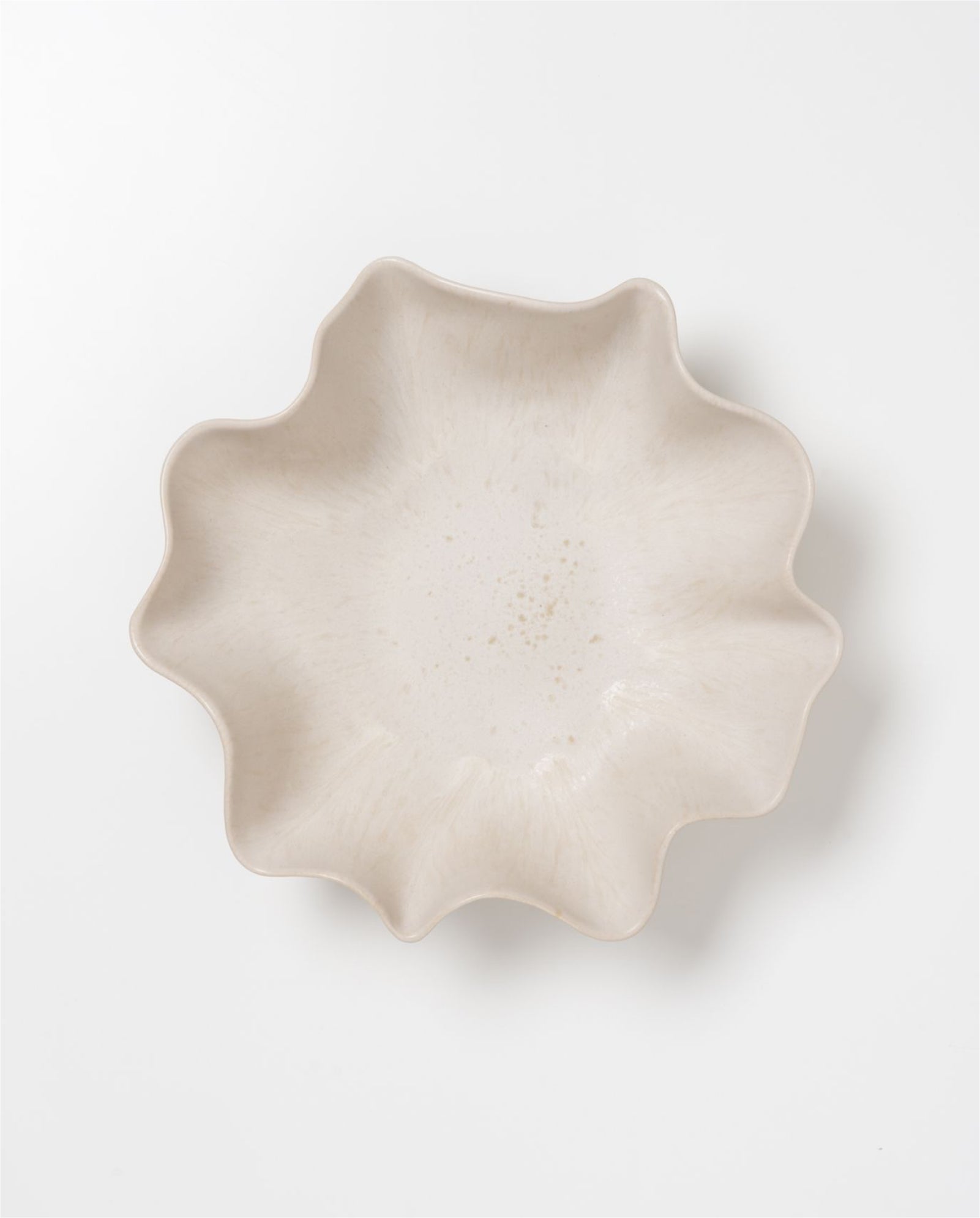 Beiger Teller mit gewelltem Rand auf weißem Hintergrund.