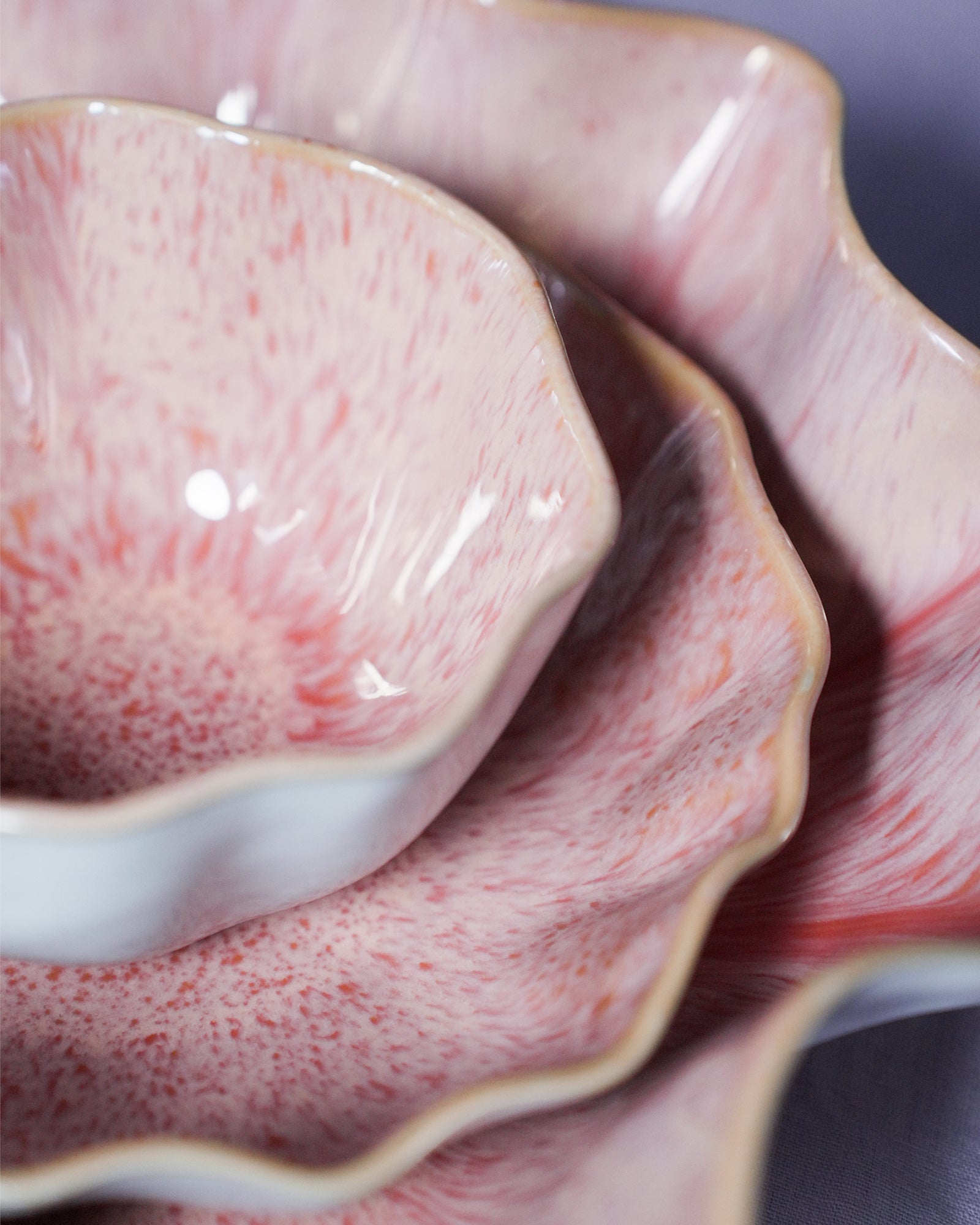 Nahaufnahme von übereinander gestapelten, rosa-weiß gefleckten Keramikschalen mit gewelltem Rand.