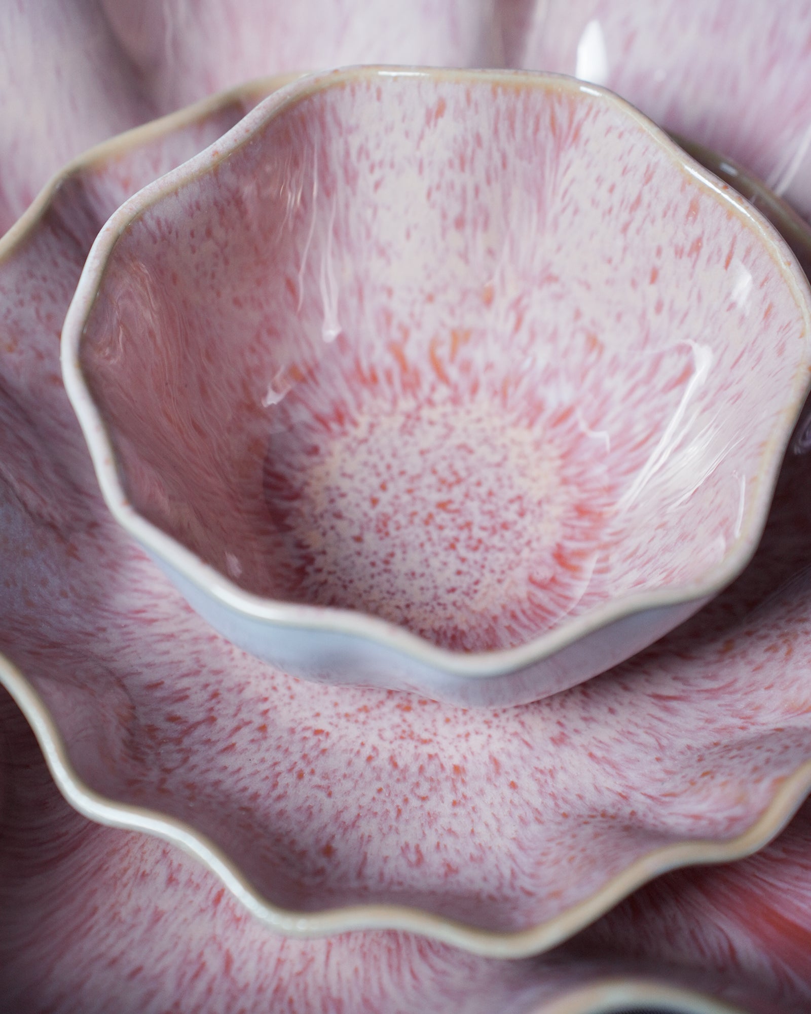 Stapel von blassrosa Keramikschalen mit gewelltem Rand und gesprenkeltem Muster.