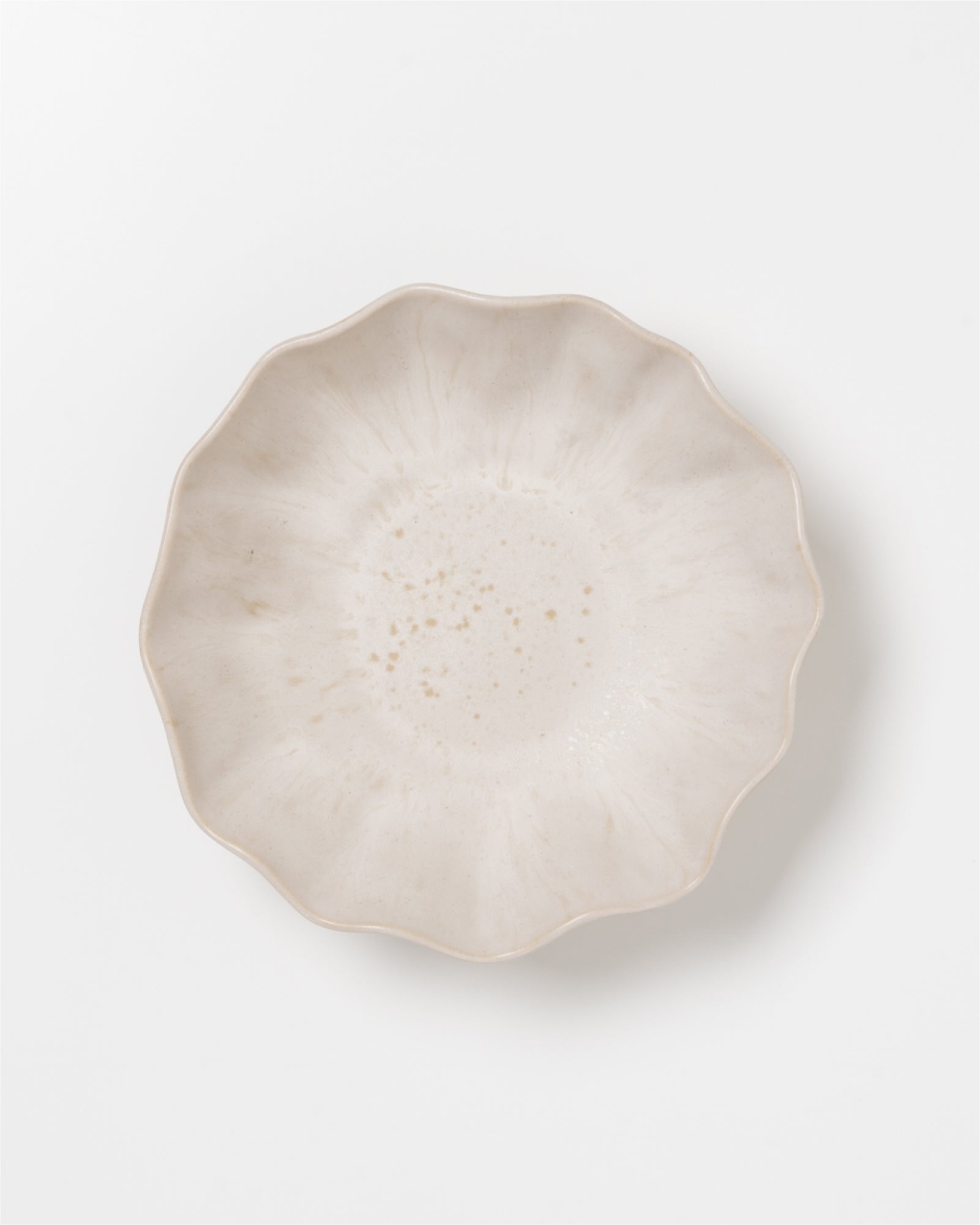 Beige, schalenförmiger Keramikteller mit gewelltem Rand und dezentem Muster auf einer weißen Oberfläche.