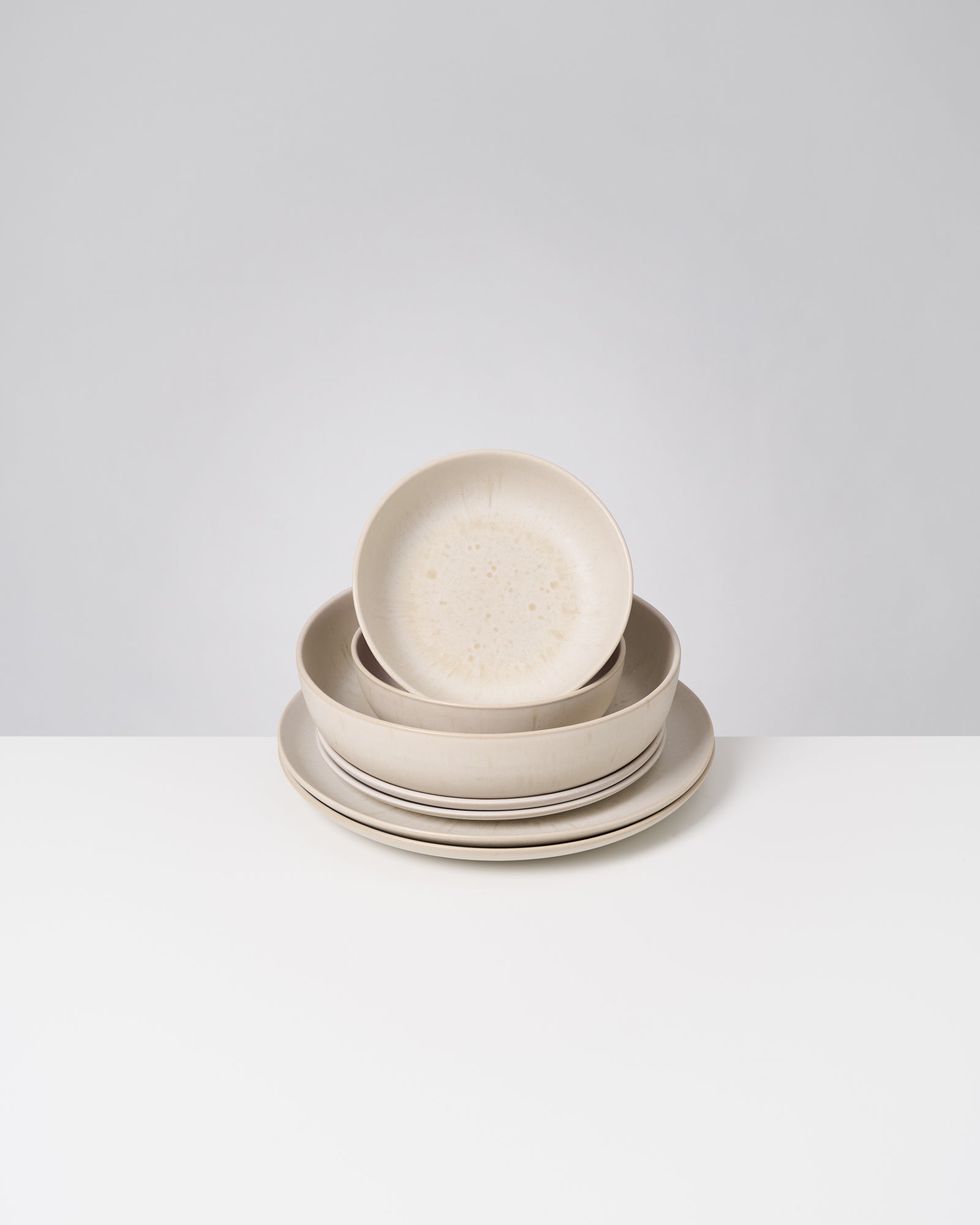 Ein Stapel aus vier beigefarbenen Tellern und einer Schüssel steht auf einem weißen Tisch.