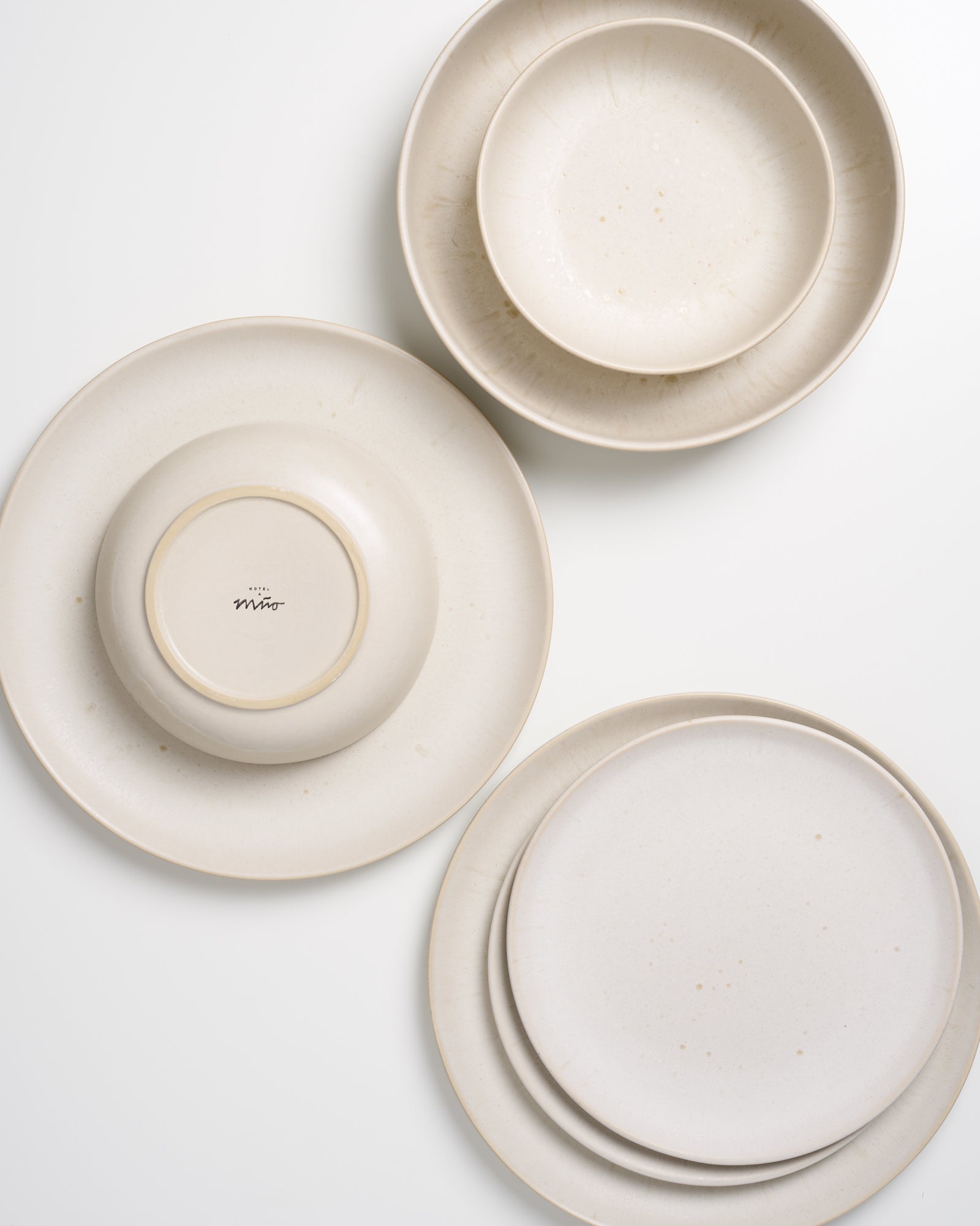 Drei hellbeige Teller und zwei Schalen auf weißem Hintergrund, ein Teller mit Markierung "mio" auf der Unterseite.
