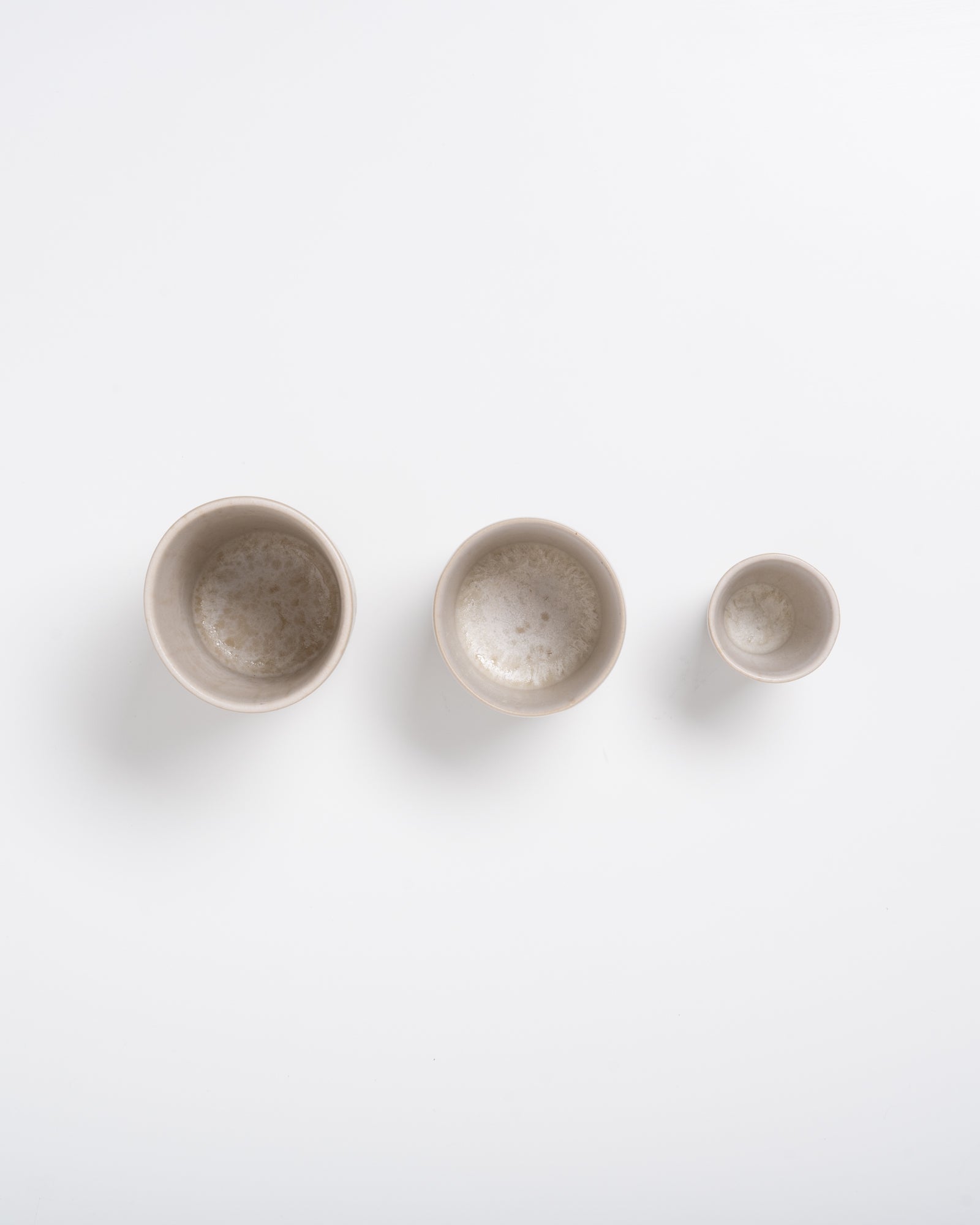 Drei unterschiedlich große, leere, cremefarbene Schalen auf weißem Hintergrund.