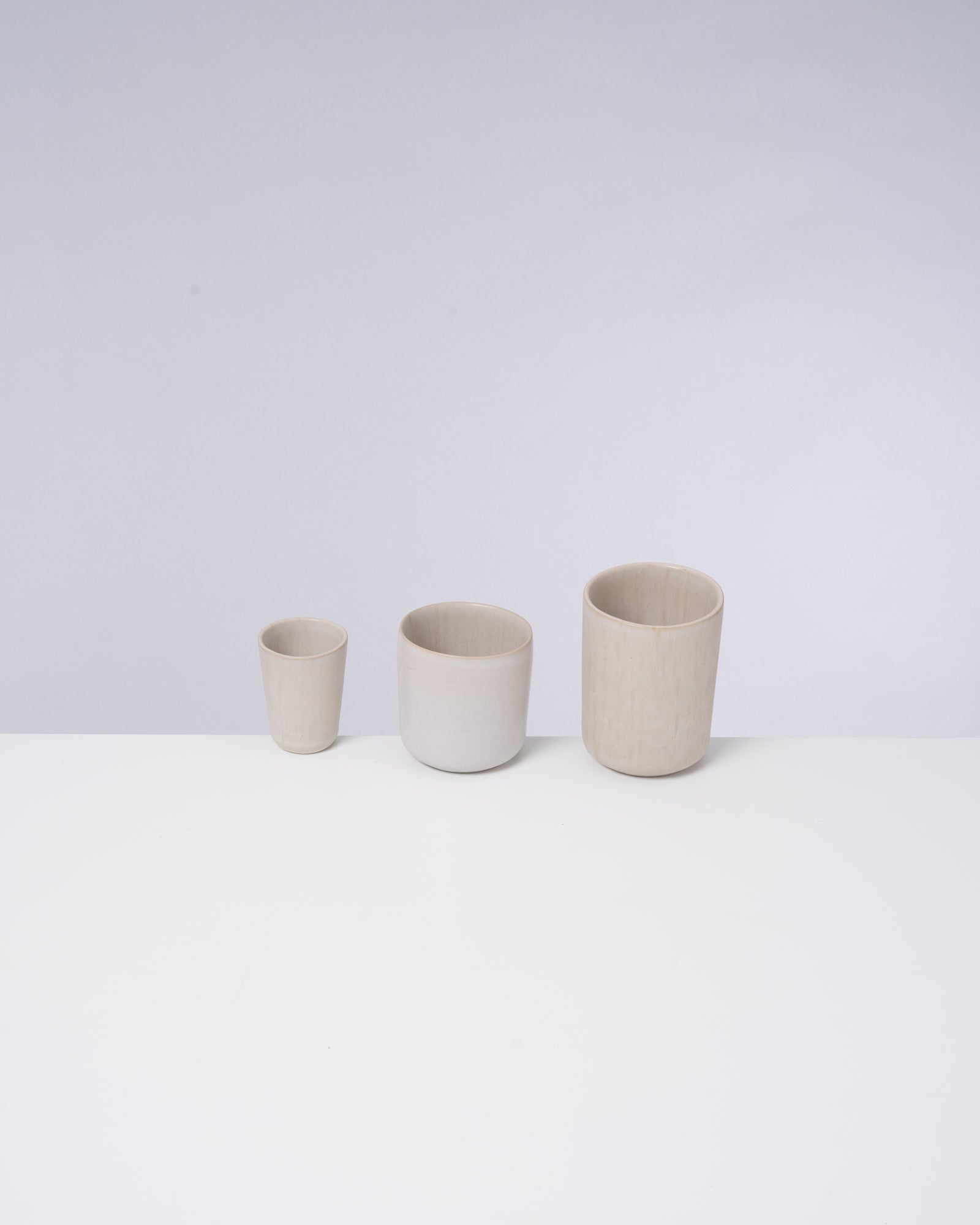 Drei unterschiedlich große, hellbraune, zylindrische Gefäße stehen nebeneinander auf einer weißen Oberfläche.