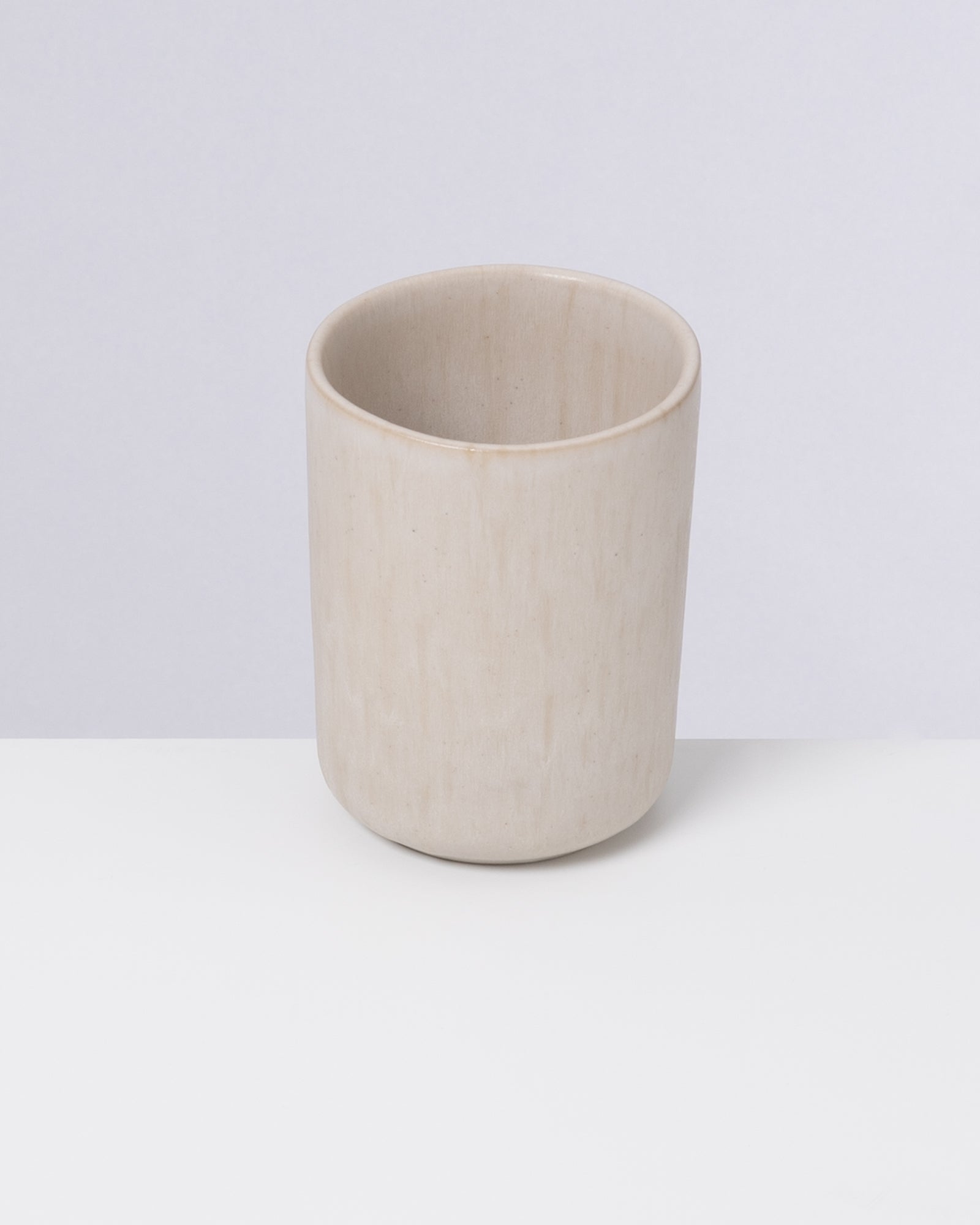 Ein becherförmiger, hellbeiger Keramikbecher auf weißem Hintergrund.