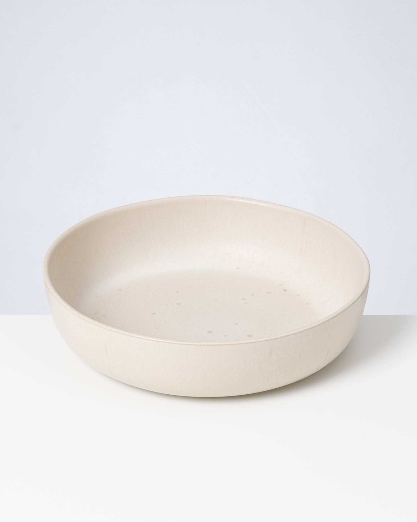 Beiger, flacher Keramikteller auf einem weißen Hintergrund.