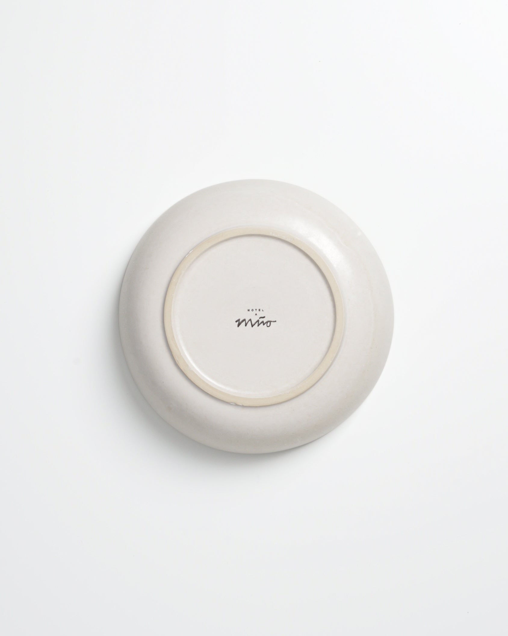 Unterseite eines hellen Tellers mit schwarzem Schriftzug "Hotel Miro" in der Mitte, auf einem weißen Hintergrund.