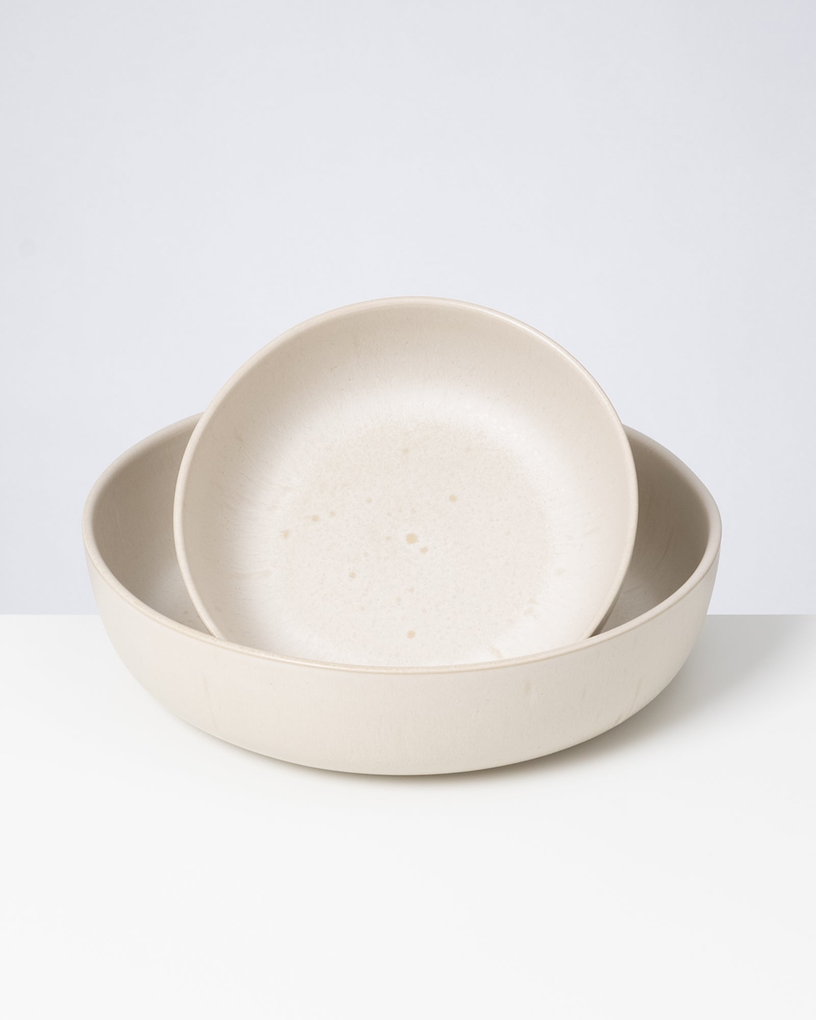 Zwei übereinander gestapelte, cremefarbene Schalen auf weißem Hintergrund.