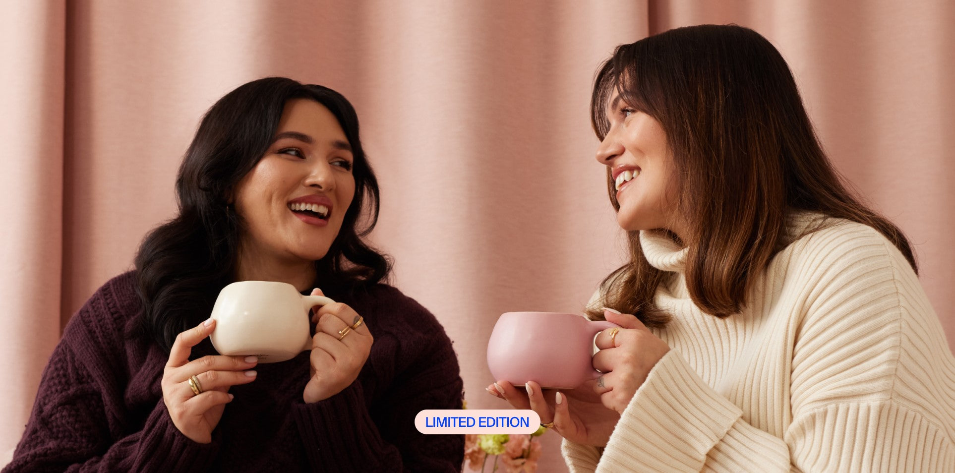 Zwei Frauen lächeln sich an und halten Tassen in der Hand, vor einem rosa Hintergrund mit "Limited Edition"-Text.