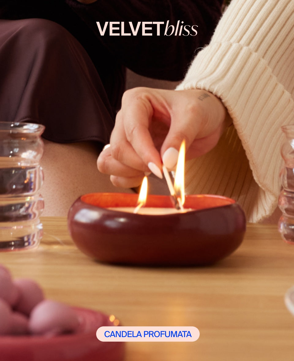 Eine Hand zündet eine runde Duftkerze auf einem Tisch an, neben Glas und Dekoration.