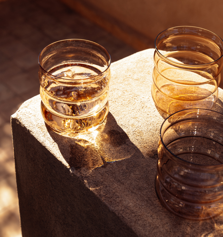 Drei leere Glasbecher stehen auf einem steinernen Podest in der Sonne.