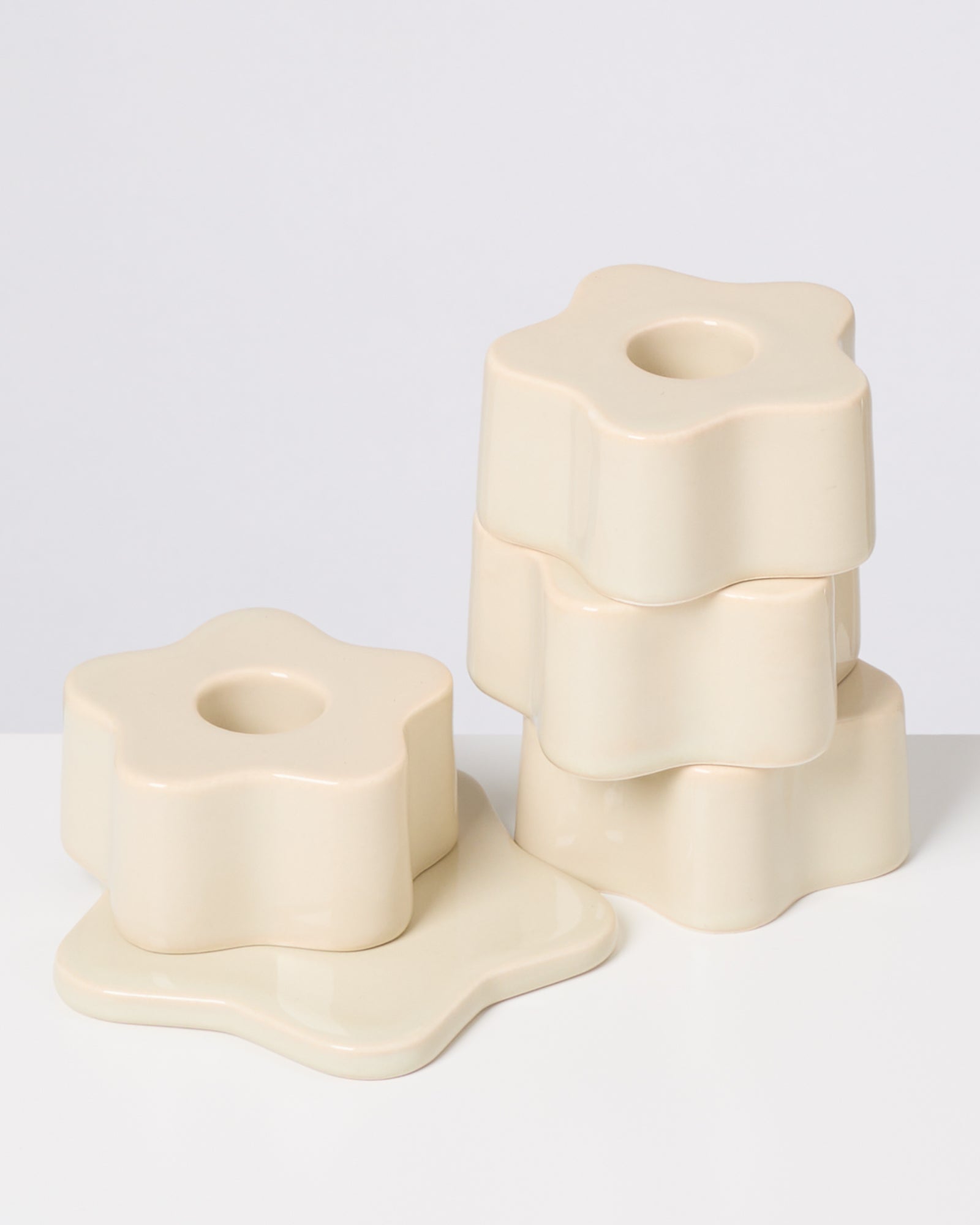 Beige, blumenförmige Kerzenhalter, teils gestapelt, auf weißem Hintergrund.