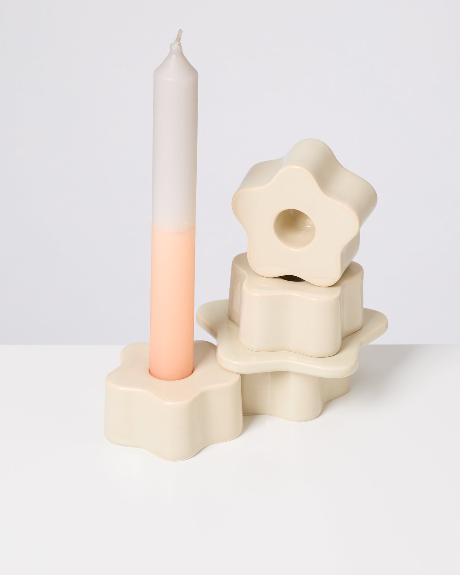 Weiße Kerze in sternförmigem Halter, daneben drei weitere gestapelte Halter auf weißem Hintergrund.