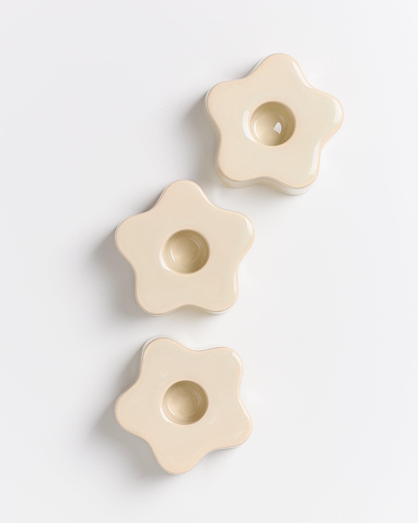 Drei beige, sternförmige Kerzenhalter aus Keramik auf weißem Hintergrund angeordnet.