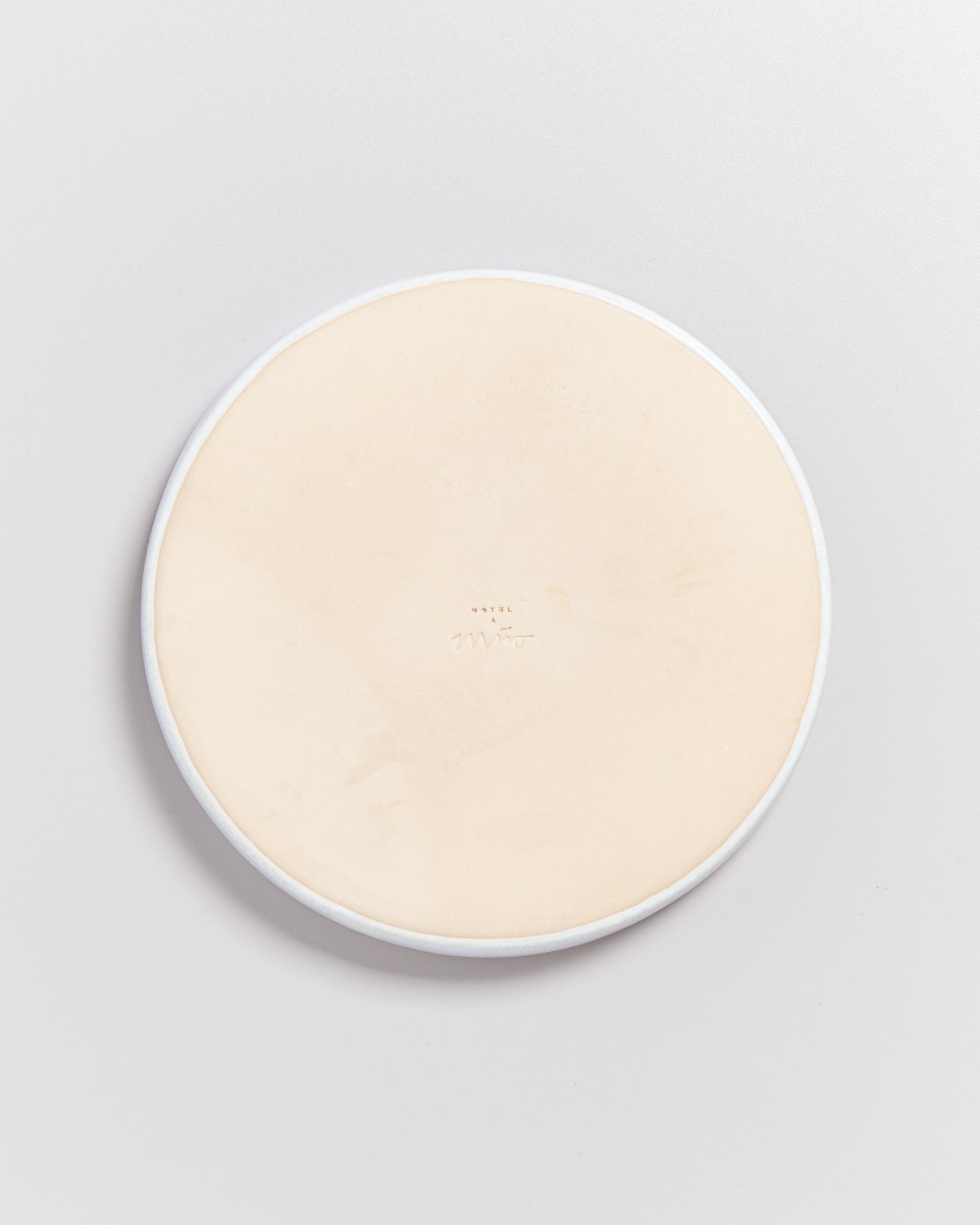 Runde, beige Keramikplatte mit einem schlichten, weißen Rand, auf einer hellgrauen Oberfläche liegend.