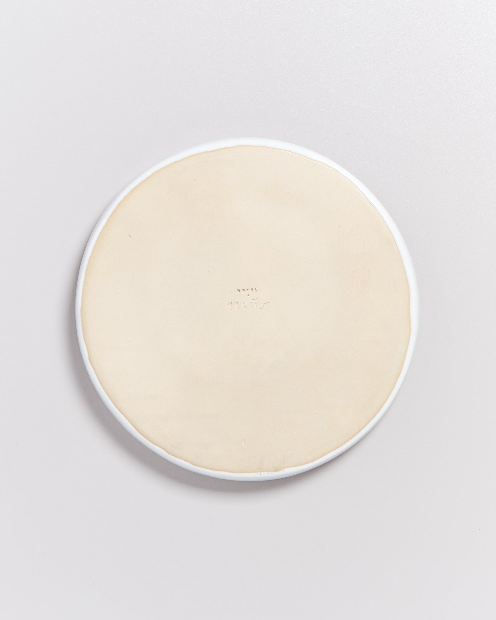 Runder, beiger Keramikteller mit weißem Rand und Aufschrift auf der Unterseite, auf weißem Hintergrund.