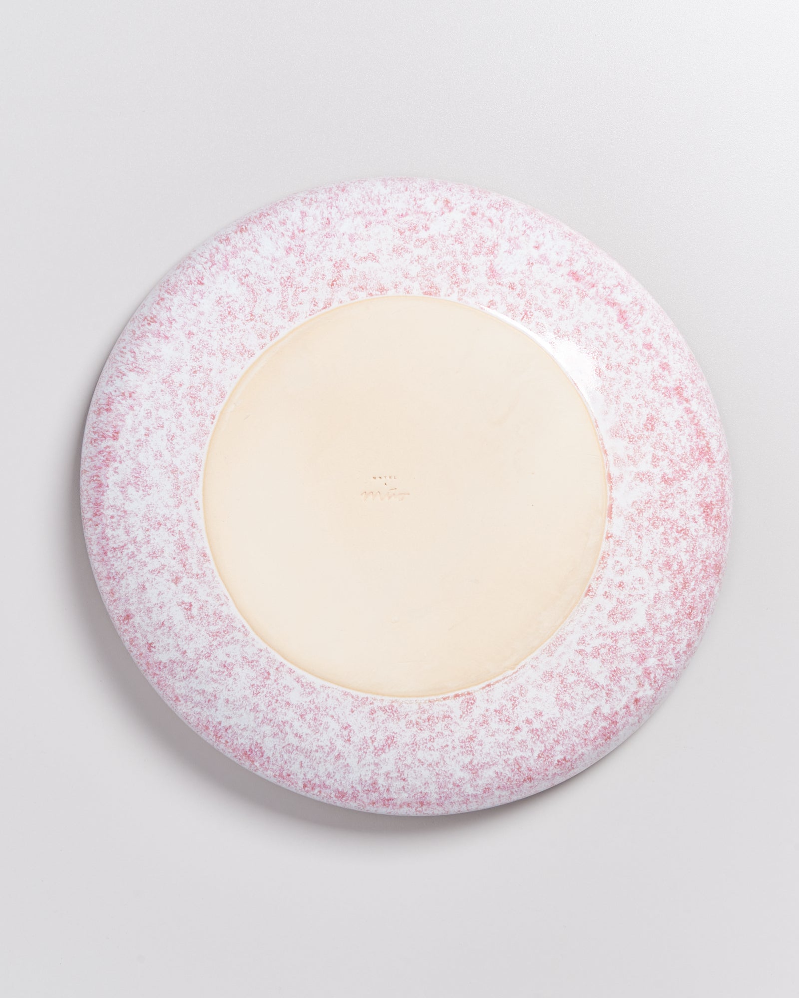 Unterseite eines runden Tellers mit beiger Mitte und rosa-weißer, gesprenkelter Verzierung am Rand.