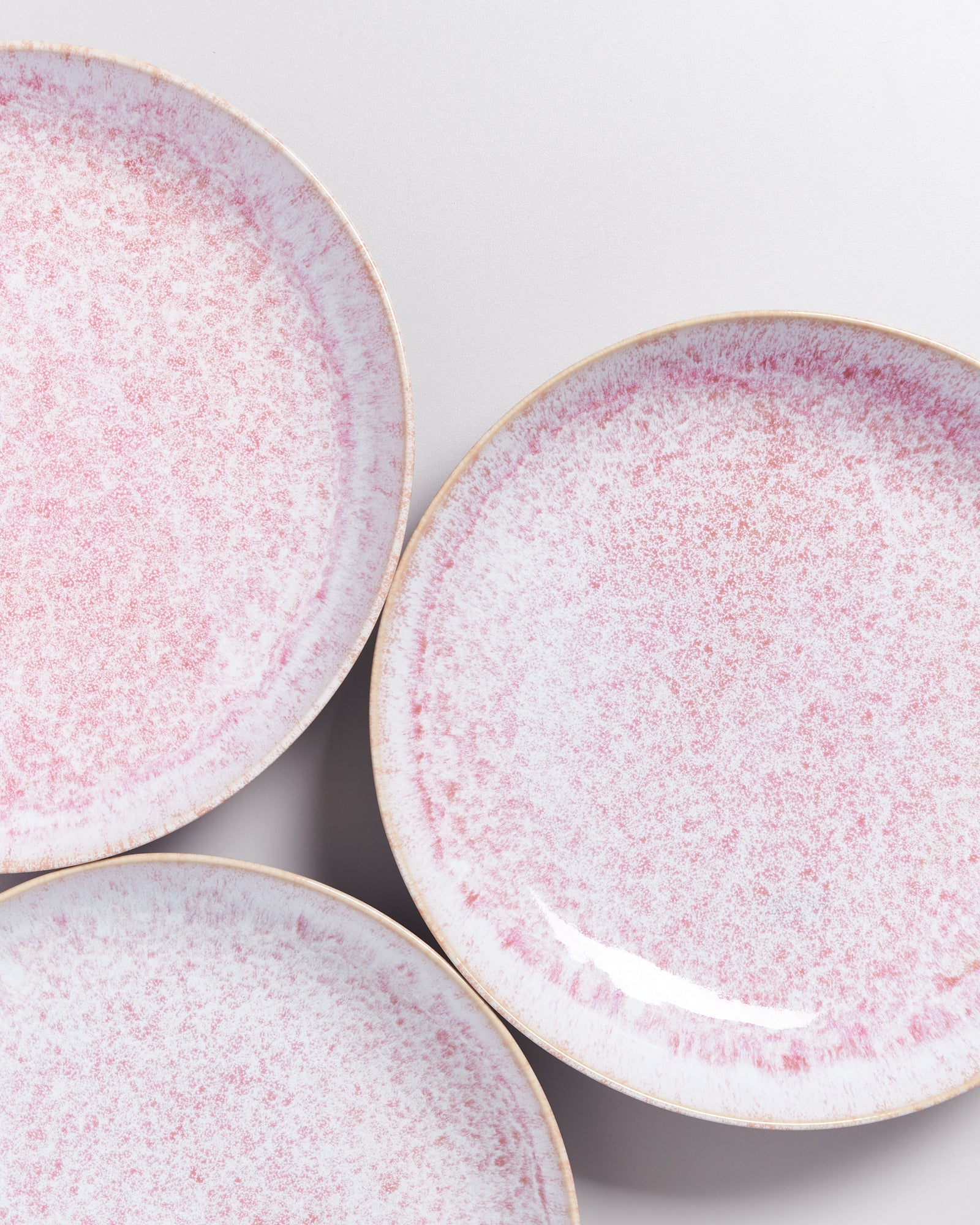 Drei rosa-weiß gesprenkelte Teller, die auf einem hellgrauen Hintergrund liegen.