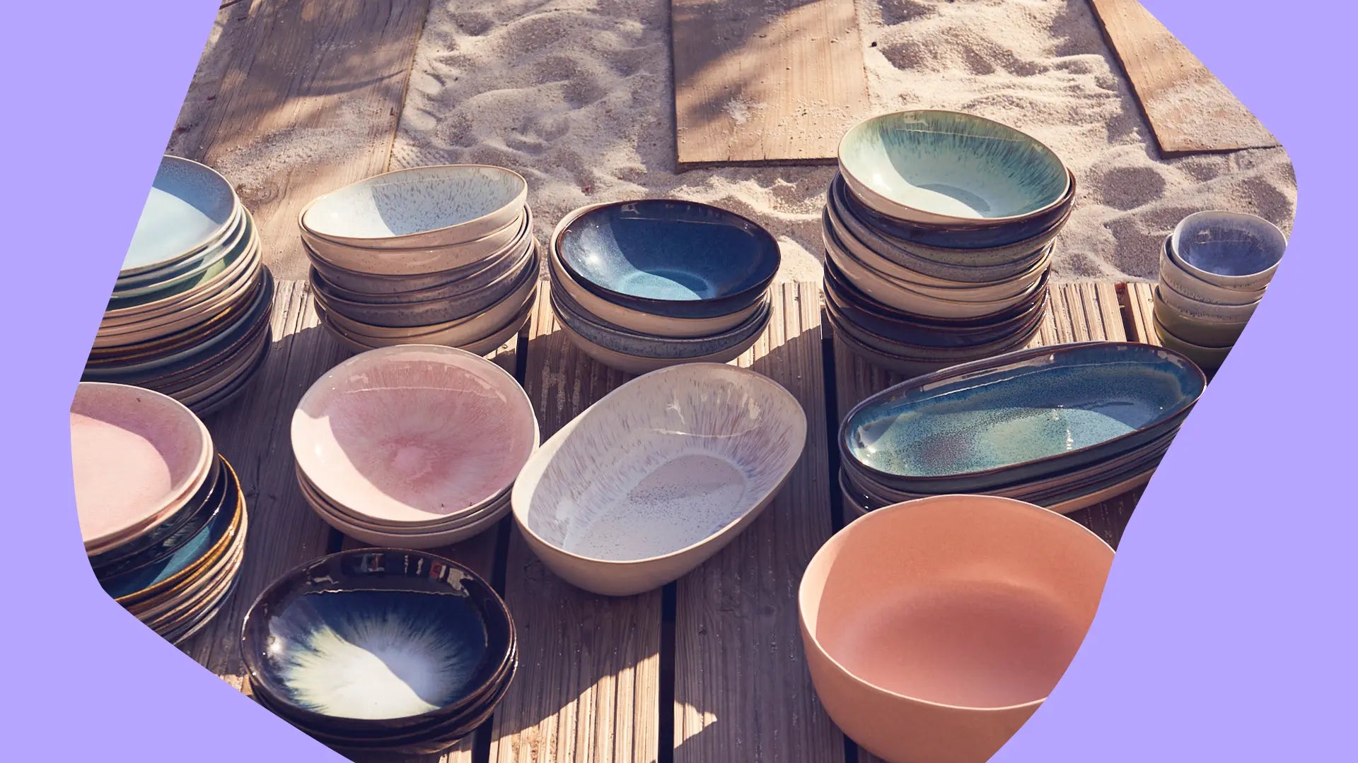 Stapel bunte Keramikschalen auf Holzterrasse, umgeben von Sand, bei Tageslicht.