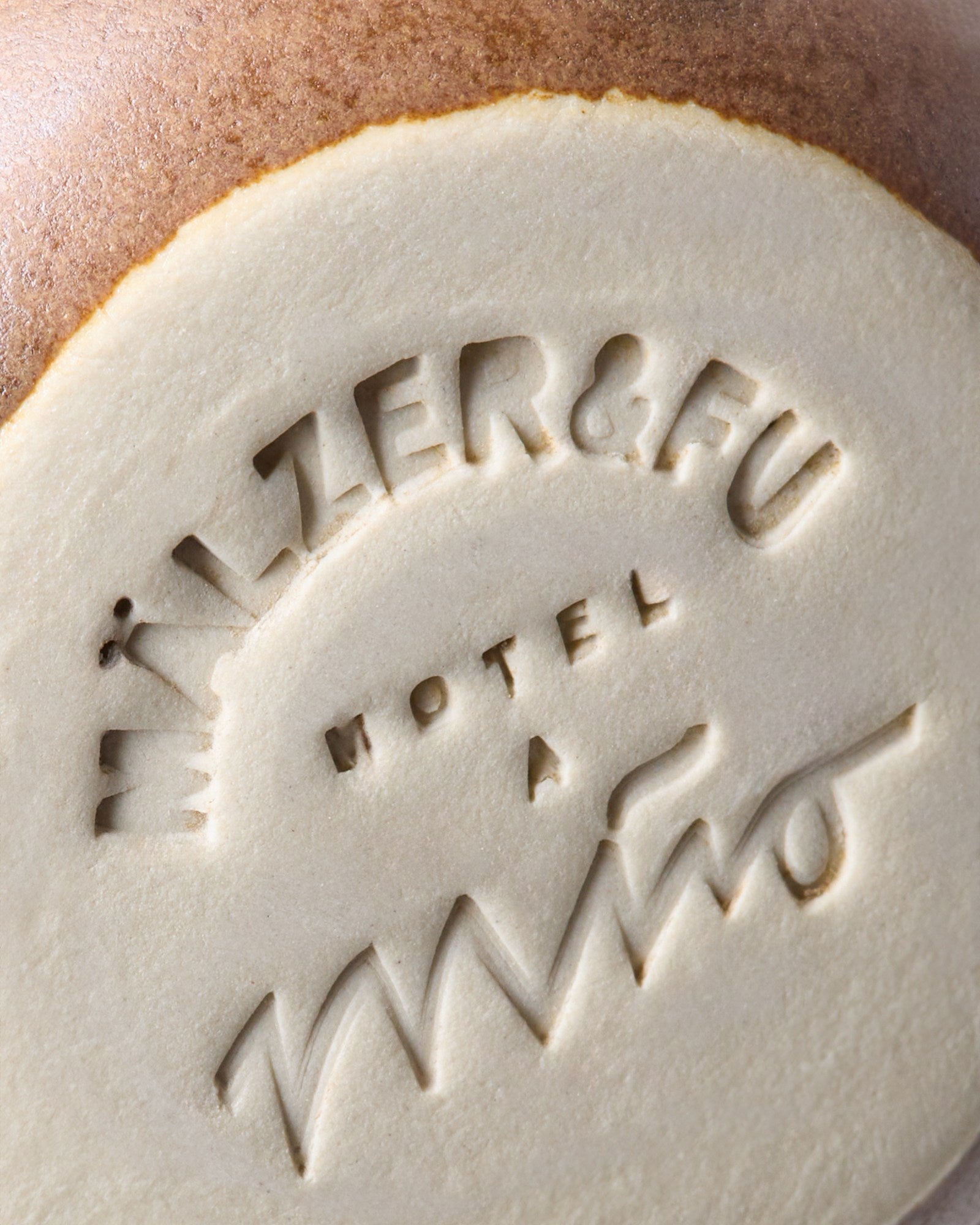 Nahaufnahme eines in Ton geprägten Schriftzugs "MÄLZER & FU HOTEL A".