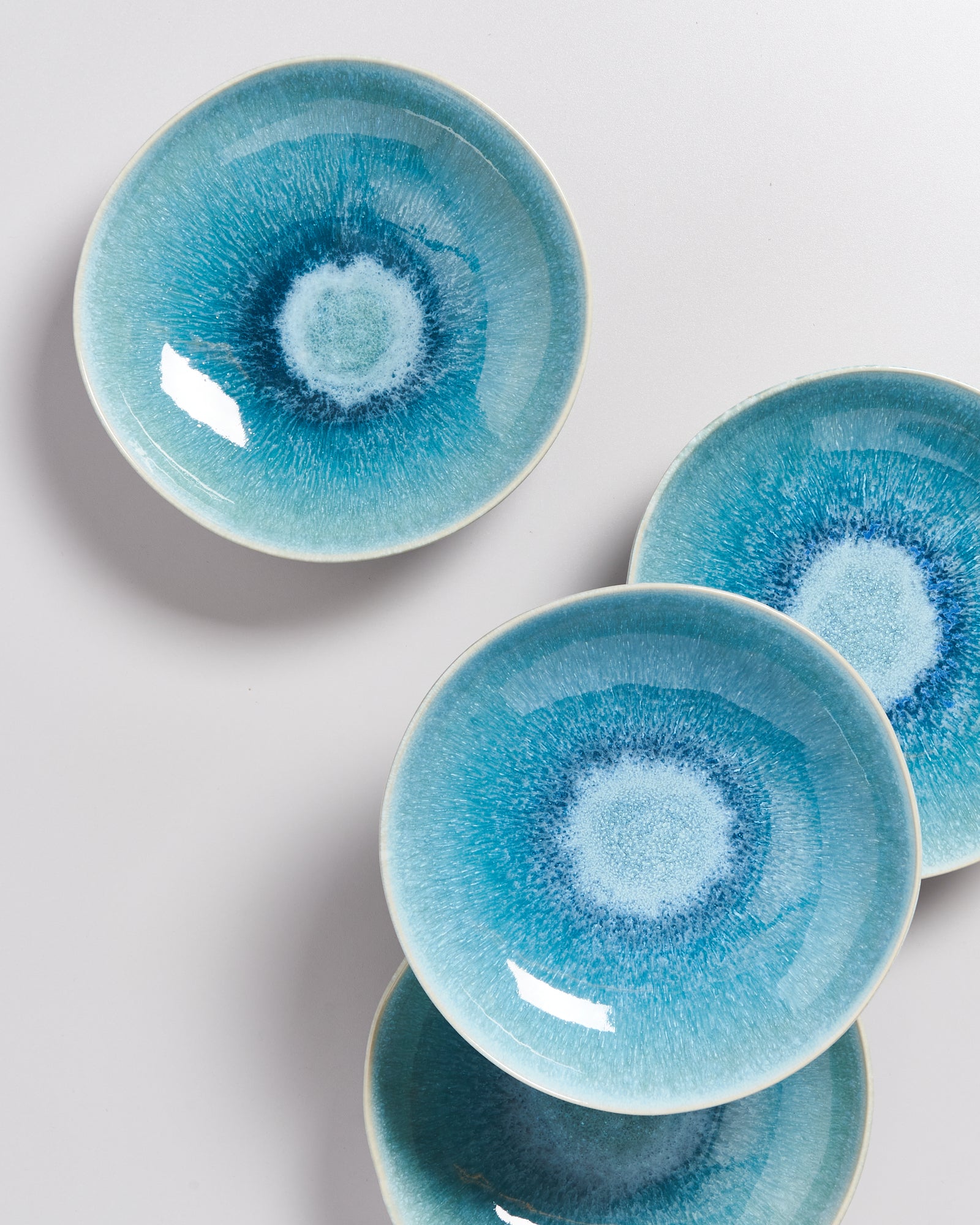 Vier blaue Keramikteller mit einem kreisförmigen Muster sind künstlerisch auf einem weißen Hintergrund arrangiert.