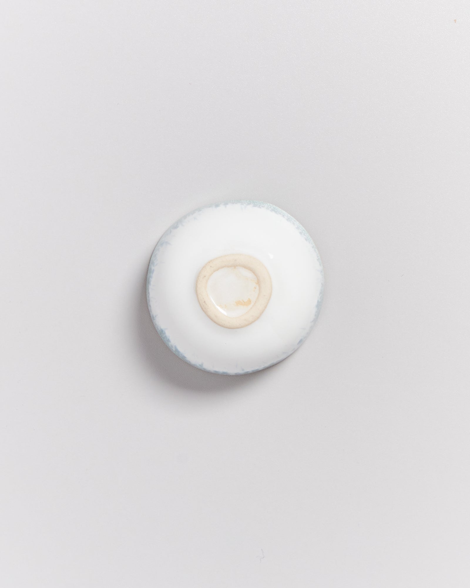 Kleiner, umgedrehter, weißer Keramikteller auf weißem Hintergrund, zeigt die unglasierte Unterseite.