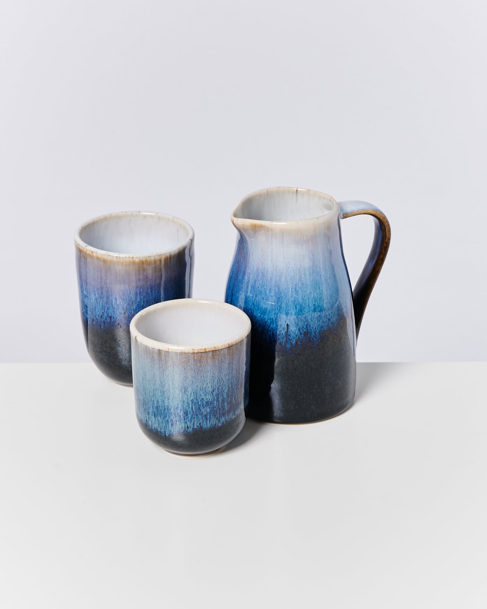 Drei blau-weiß glasierte Keramiktassen, eine mit Henkel, stehen auf einem weißen Tisch.