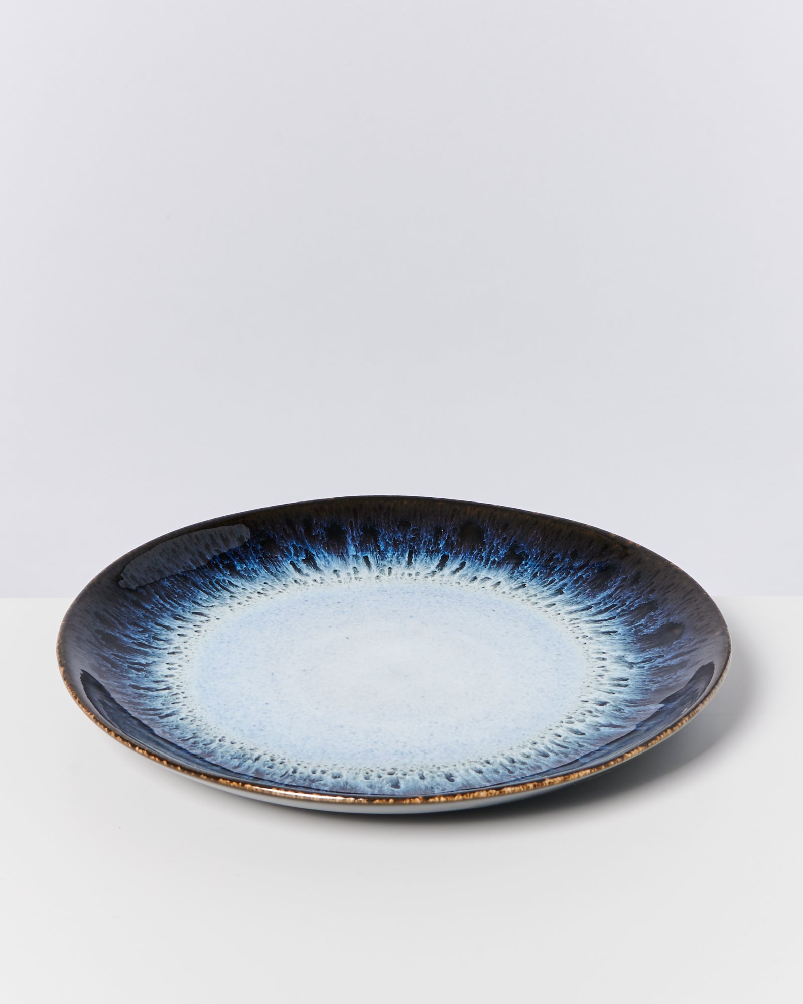 Flacher Teller mit blauem und schwarzem Muster, auf einem weißen Hintergrund liegend.