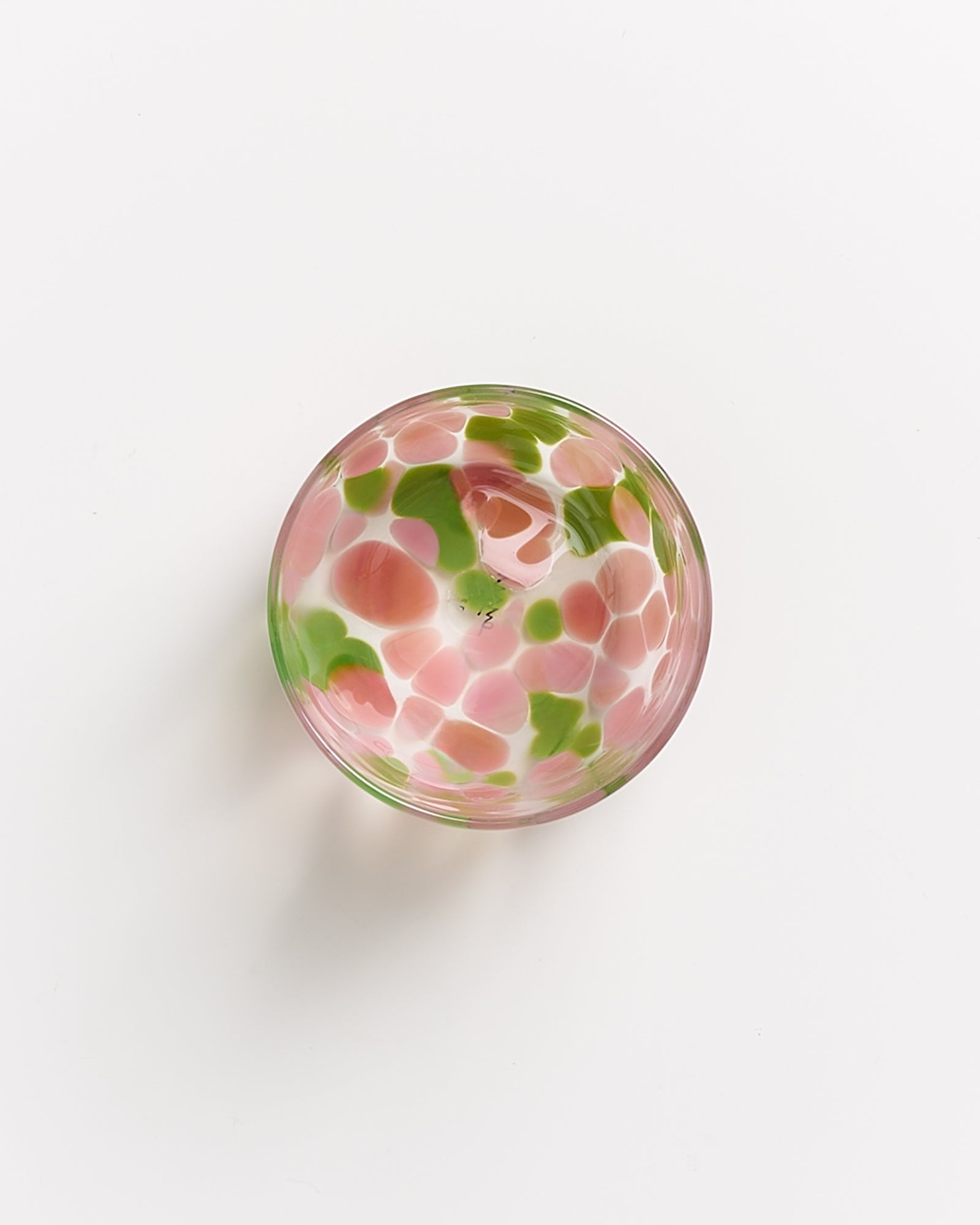 Bunte Glasschale mit rosa und grünen Mustern auf weißem Hintergrund.