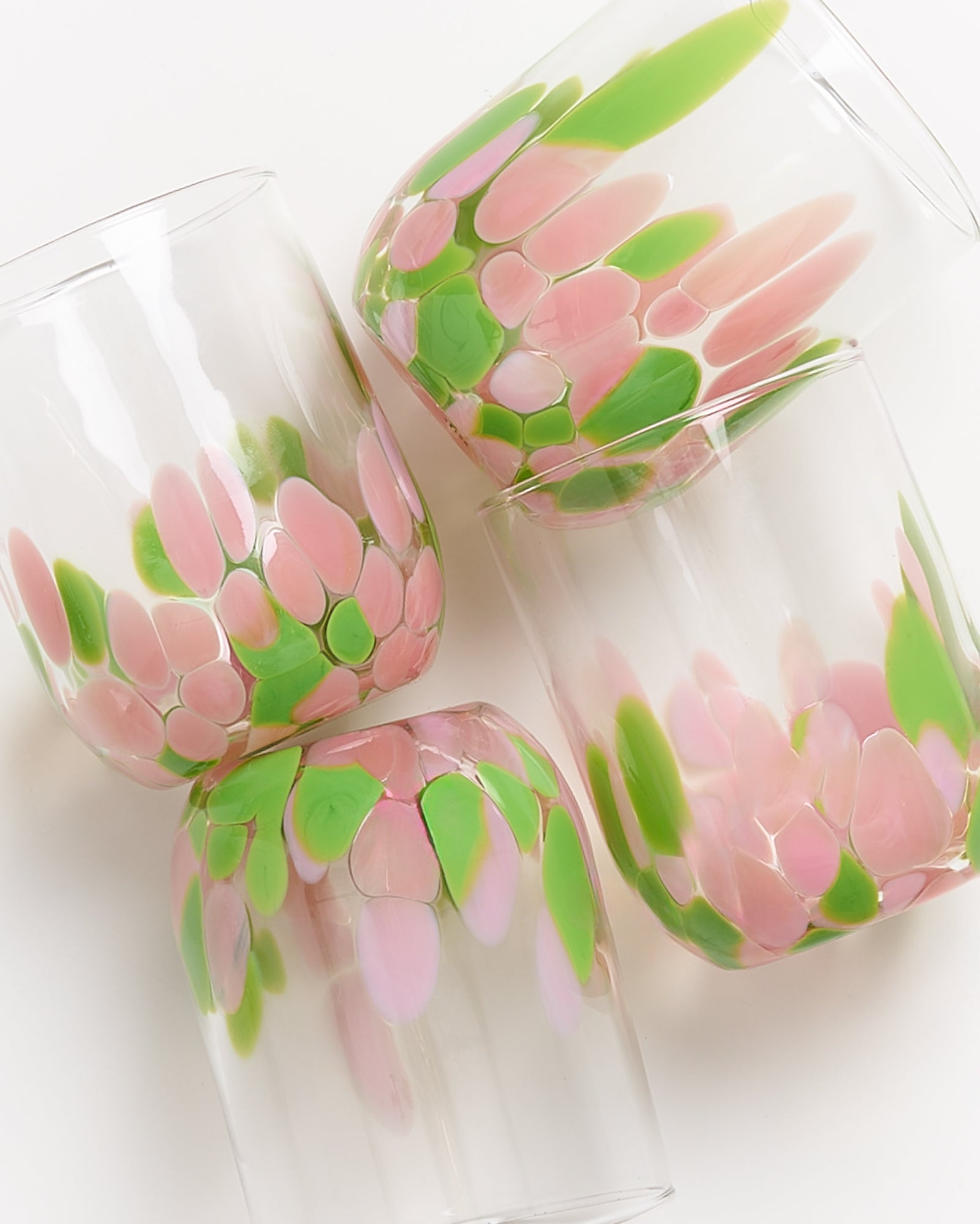 Vier Gläser mit rosa und grünen Blumenmustern liegen aufeinander auf einem weißen Hintergrund.