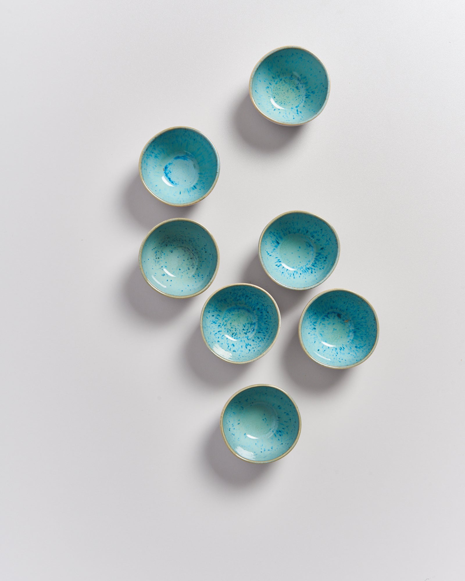 Sieben kleine, türkis gesprenkelte Schalen arrangiert auf einem weißen Hintergrund.