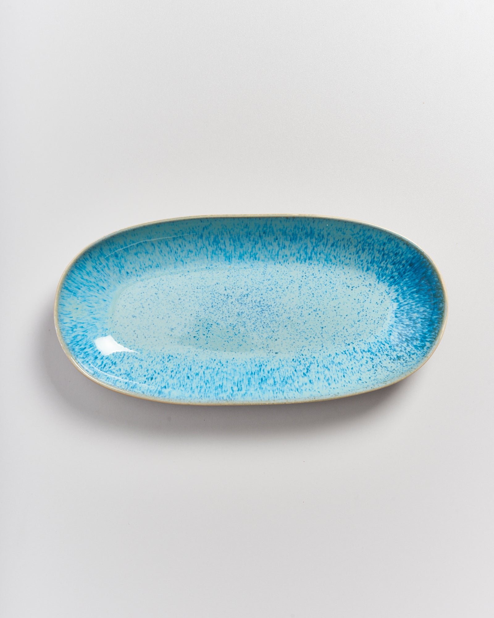 Ovale blaue Keramikplatte mit Sprenkelmuster auf hellem Hintergrund.