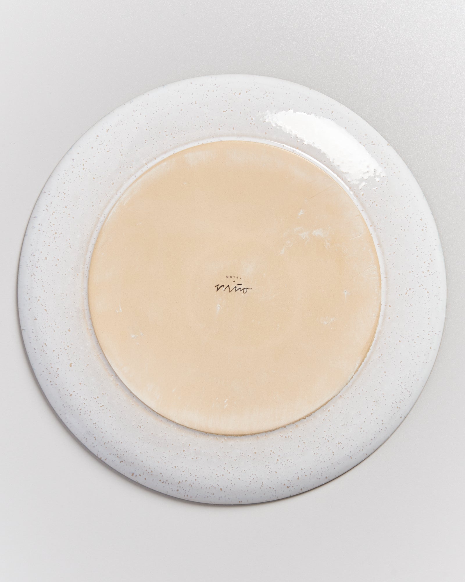 Unterseite eines Tellers mit gelblichem Zentrum und gesprenkeltem Rand auf weißem Hintergrund.