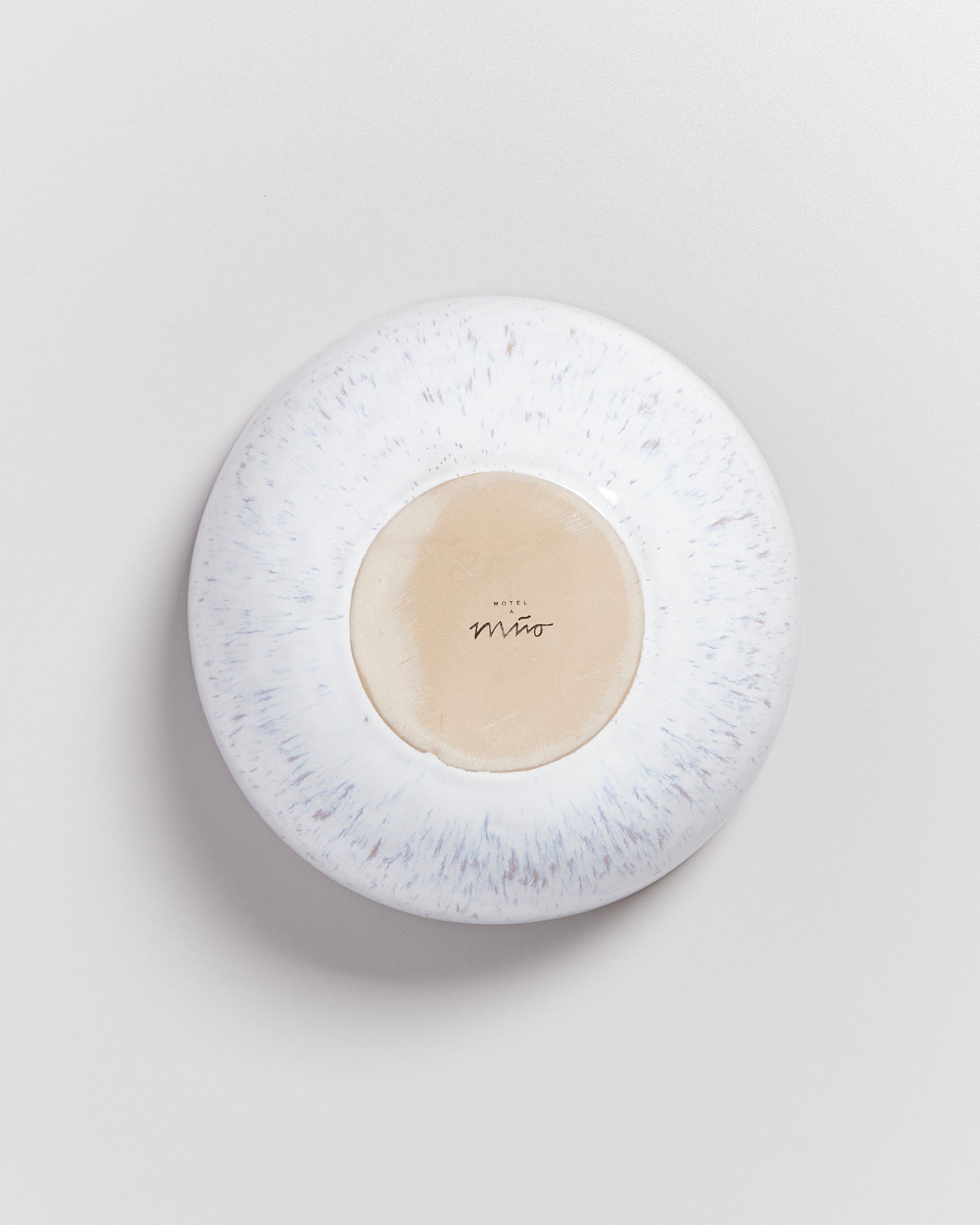 Rückseite eines Tellers mit beigem Zentrum und blauen Sprenkeln am Rand, auf hellem Hintergrund.