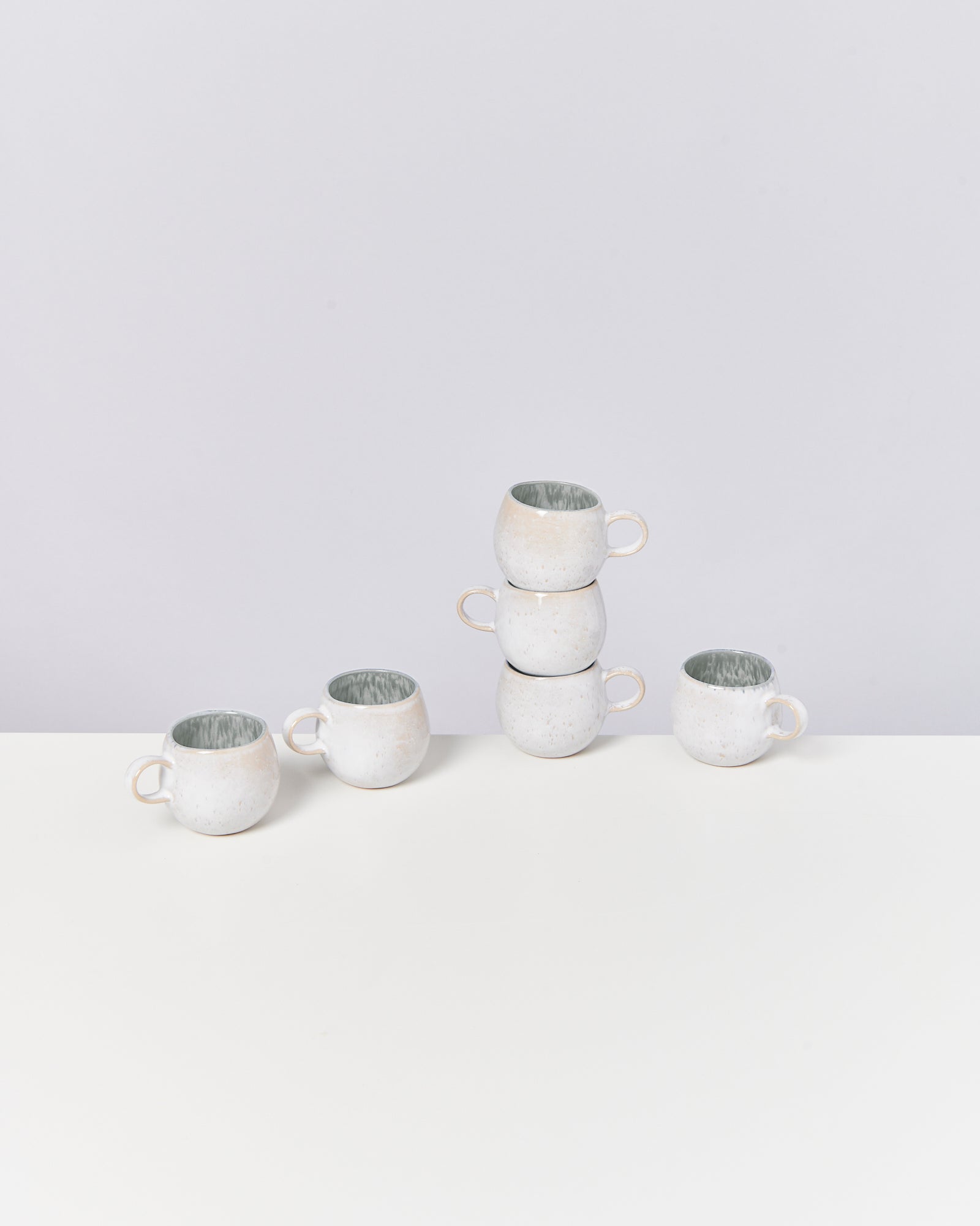 Fünf weiße Tassen auf einem Tisch, zwei gestapelt, drei nebeneinander stehend.