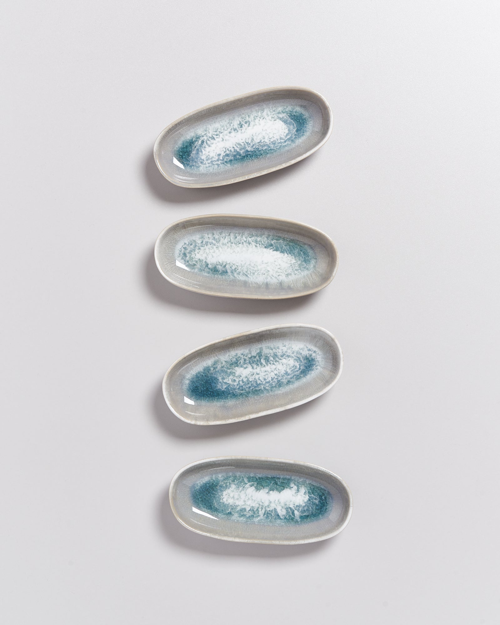 Vier ovale Keramikteller mit blau-weißen Mustern auf grauem Hintergrund.