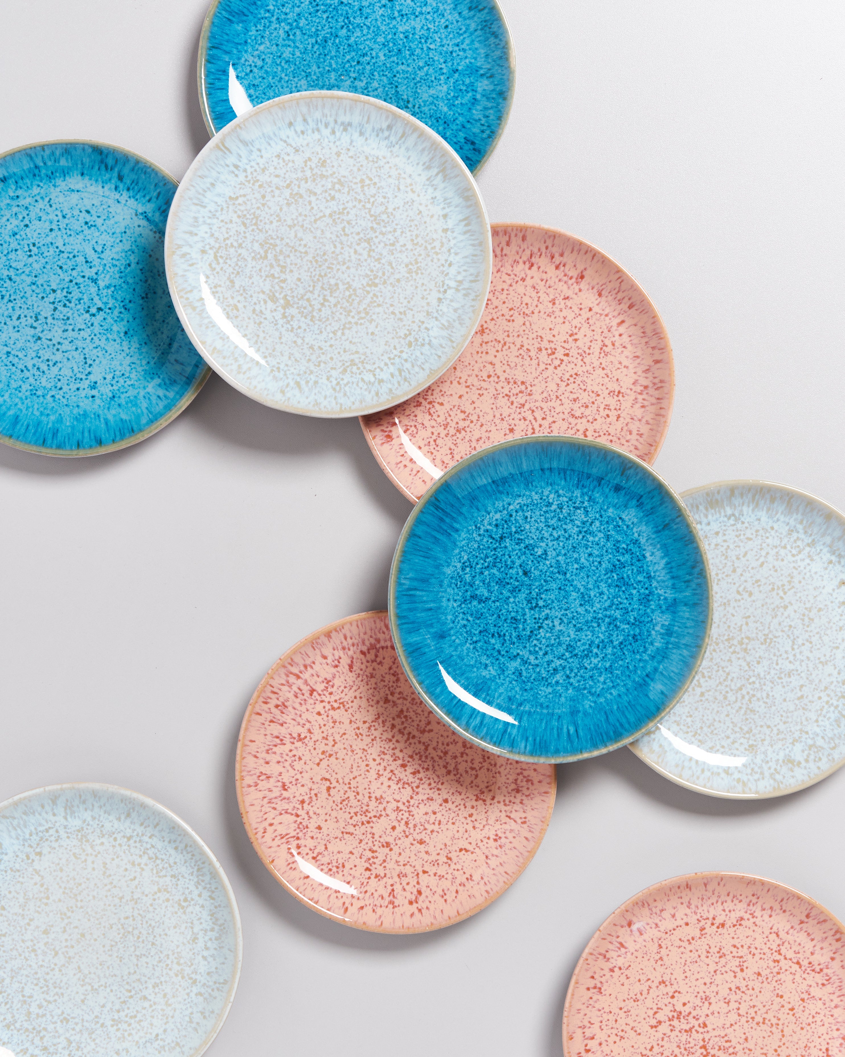 Bunte Teller in Blau, Weiß und Rosa mit gesprenkeltem Muster, auf einem hellen Hintergrund angeordnet.