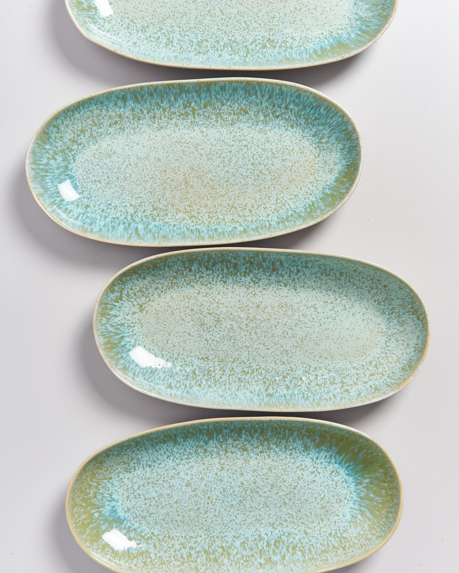 Vier ovale Teller mit blauer und grüner gesprenkelter Glasur auf weißem Hintergrund.