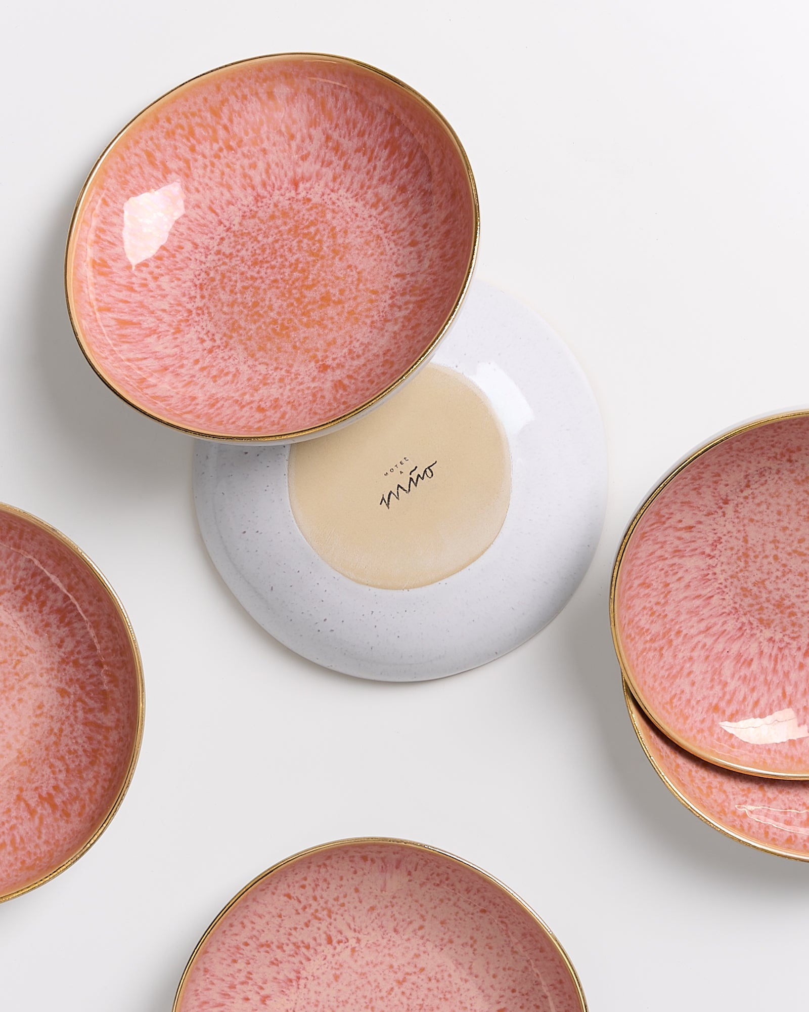 Sechs runde, rosafarbene Keramikteller mit goldenen Rändern, einer umgedreht mit sichtbarer Unterseite.