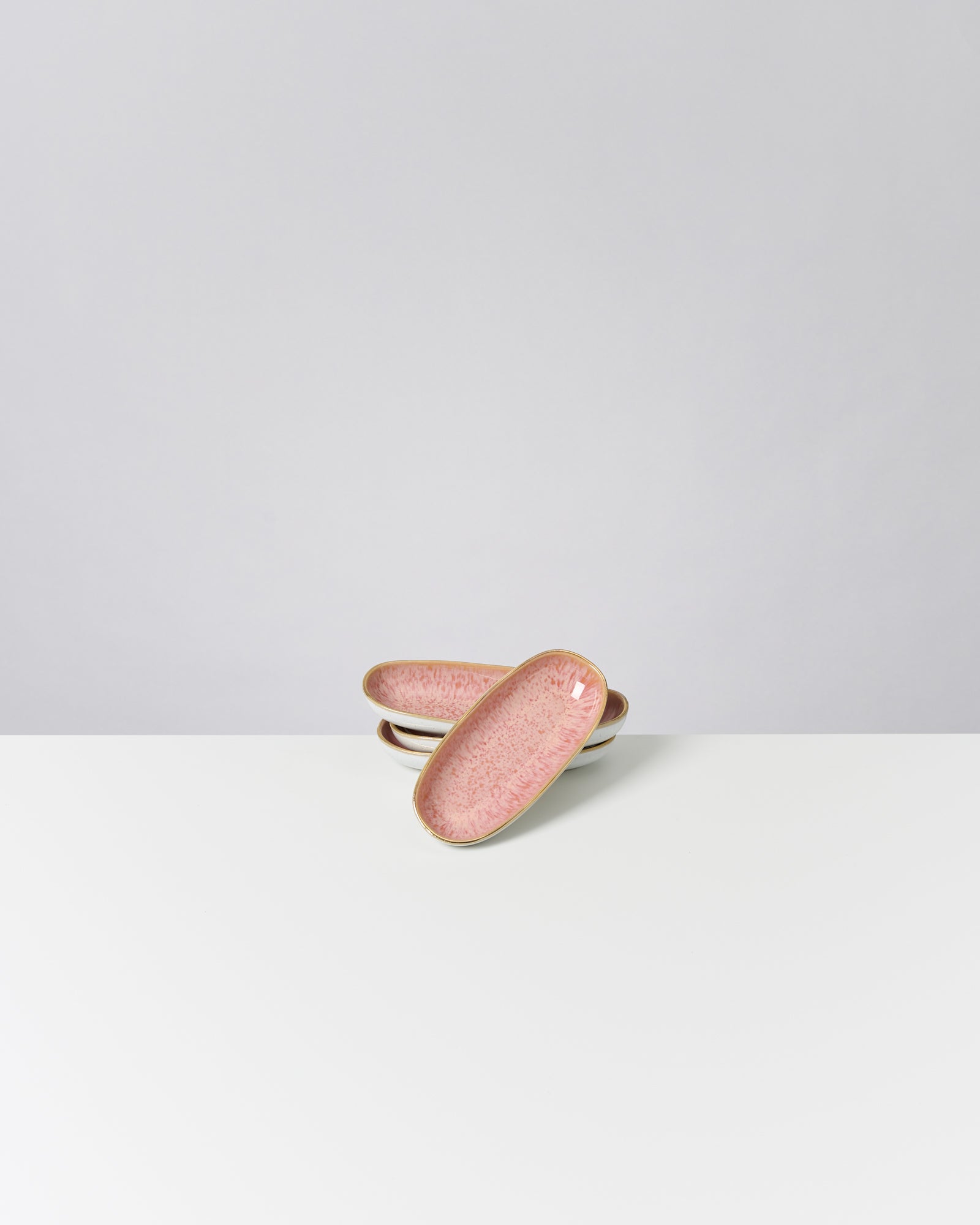 Zwei rosafarbene ovale Keramikschalen auf einer weißen Oberfläche vor einem grauen Hintergrund.