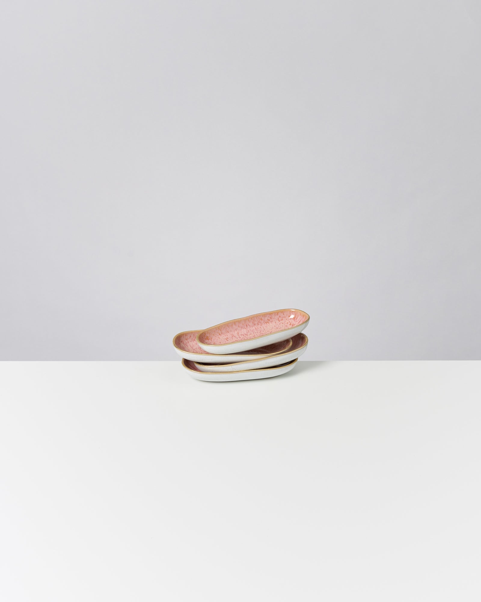 Drei gestapelte ovale Keramikschalen mit rosa Innenseiten auf einer weißen Oberfläche vor grauem Hintergrund.